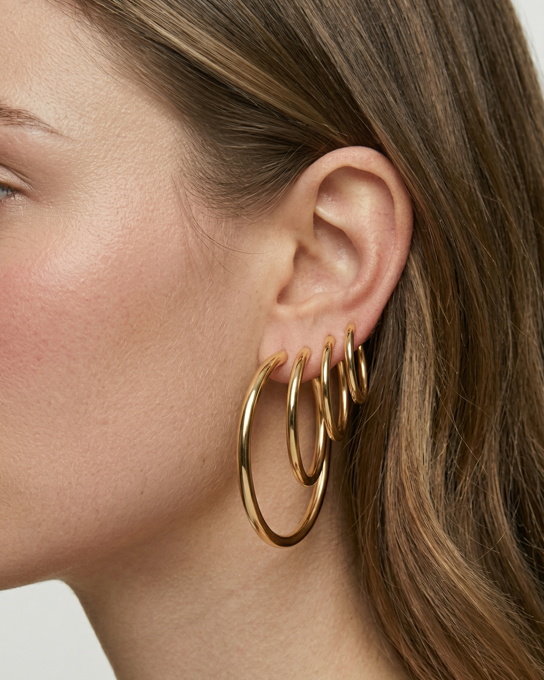 Close-up of a person wearing gold hoop earrings with a neutral background