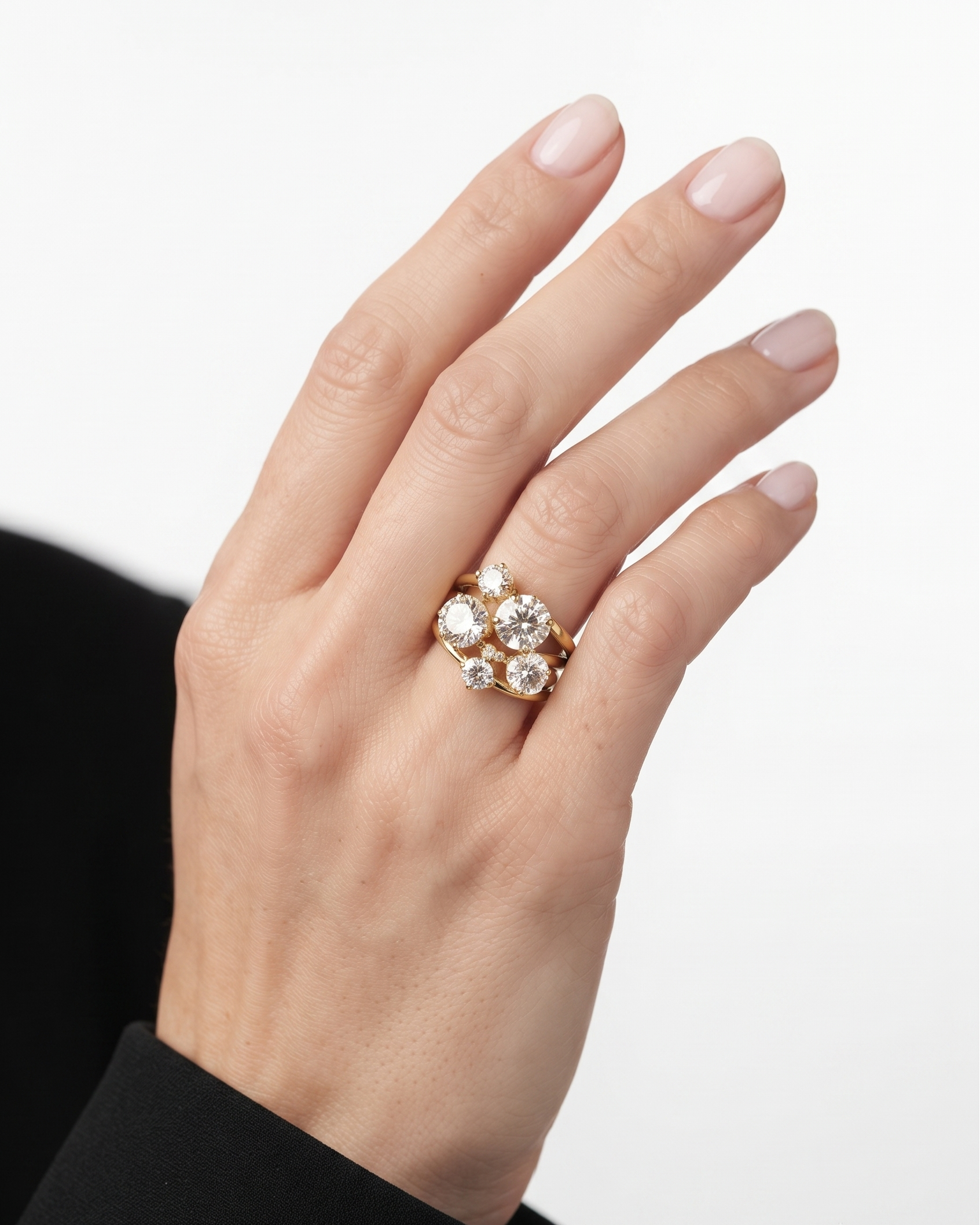 A close-up of a hand wearing a gold ring with a cluster of clear gemstones, set against a clean white background.