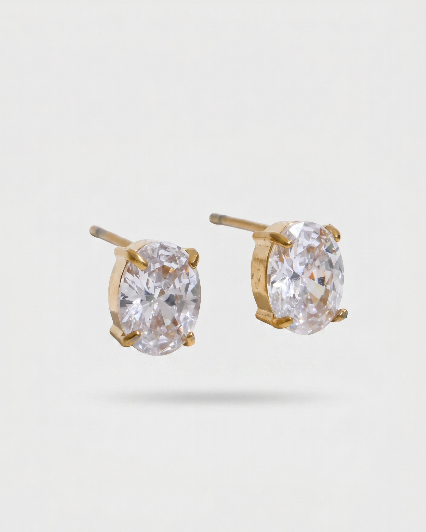 Gold earrings with clear gemstones on a light gray background