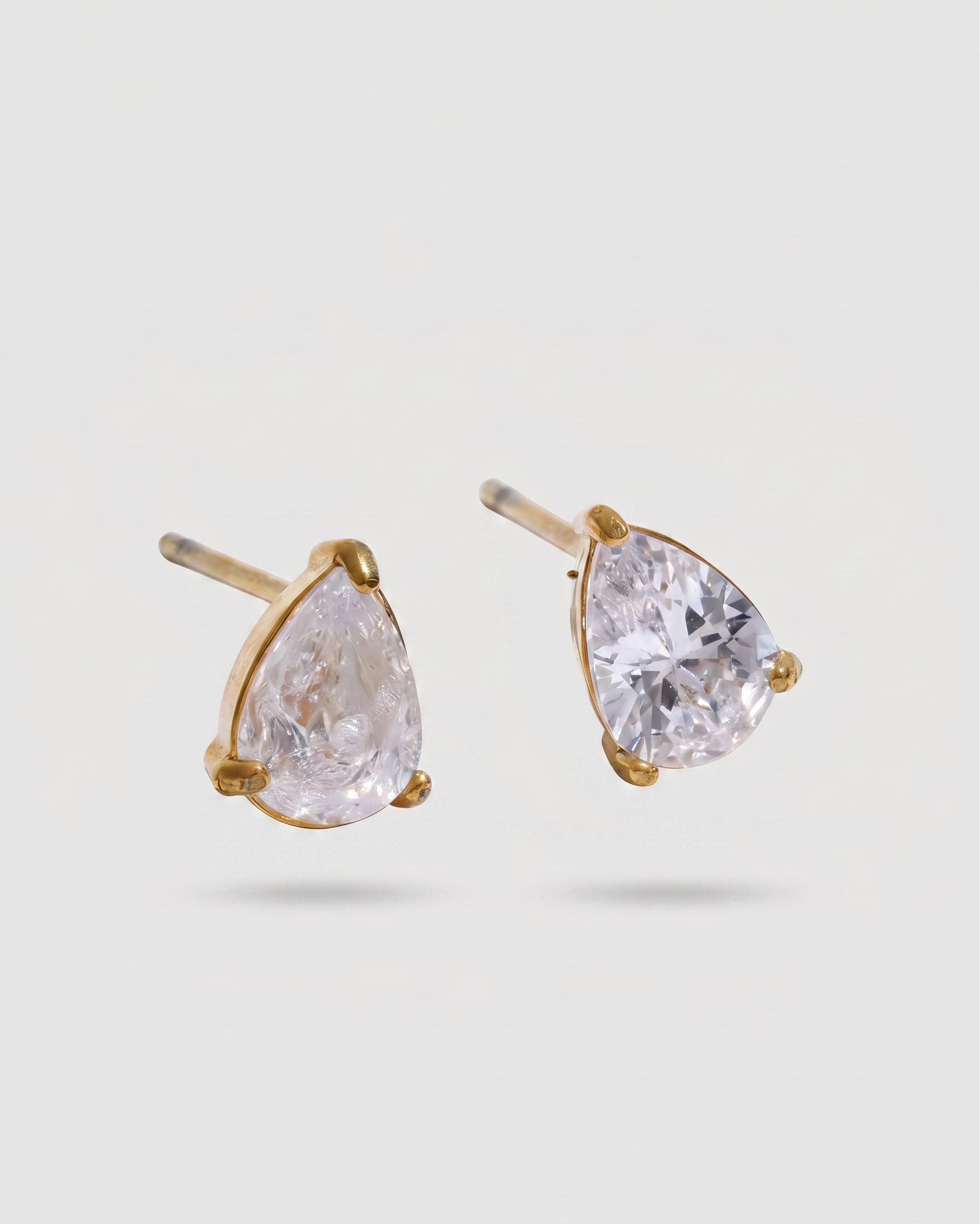 Pair of gold earrings with clear teardrop-shaped gemstones on a light gray background