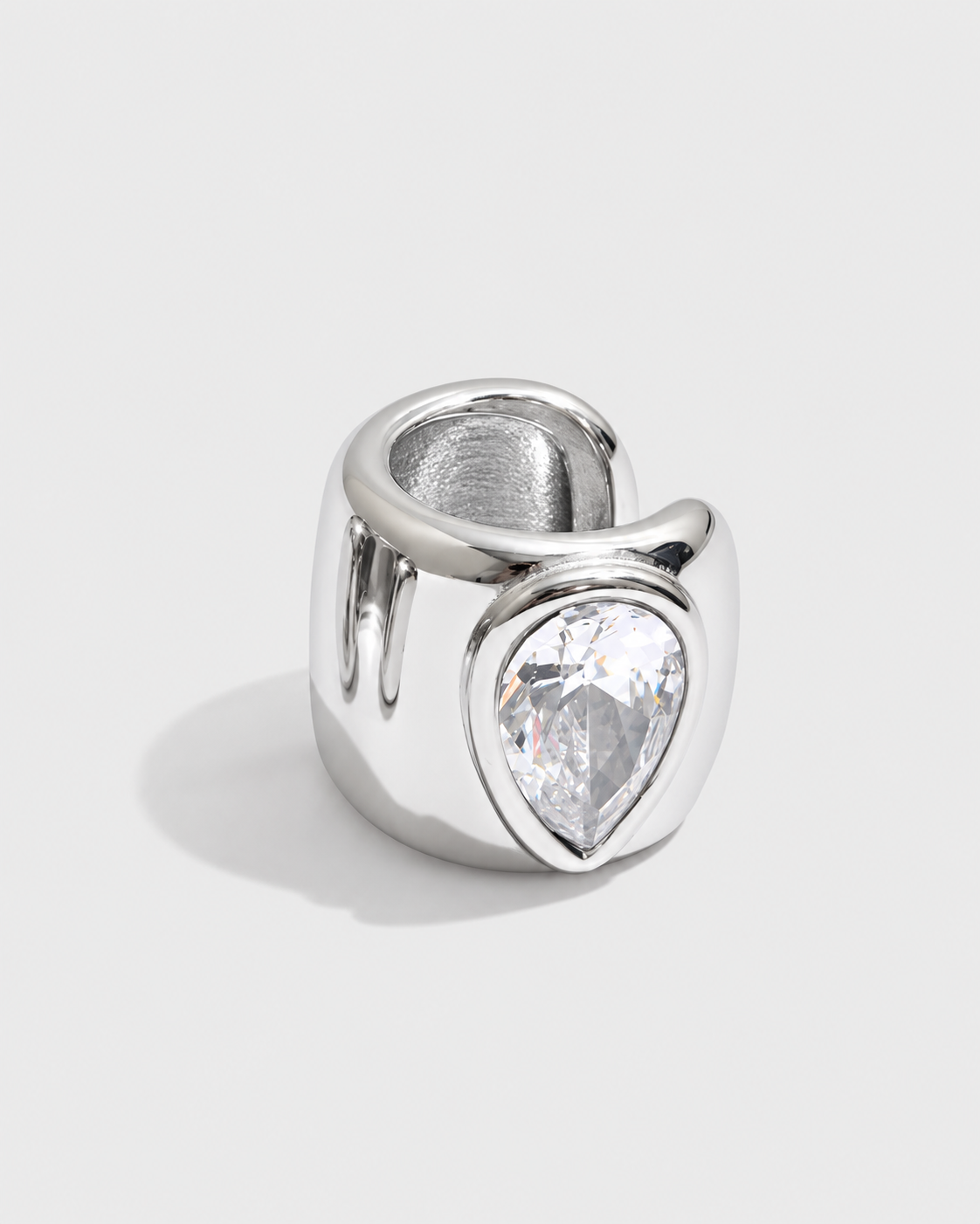 A silver-toned ring featuring a large, teardrop-shaped clear gemstone in a prong setting, photographed on a clean, light gray background.