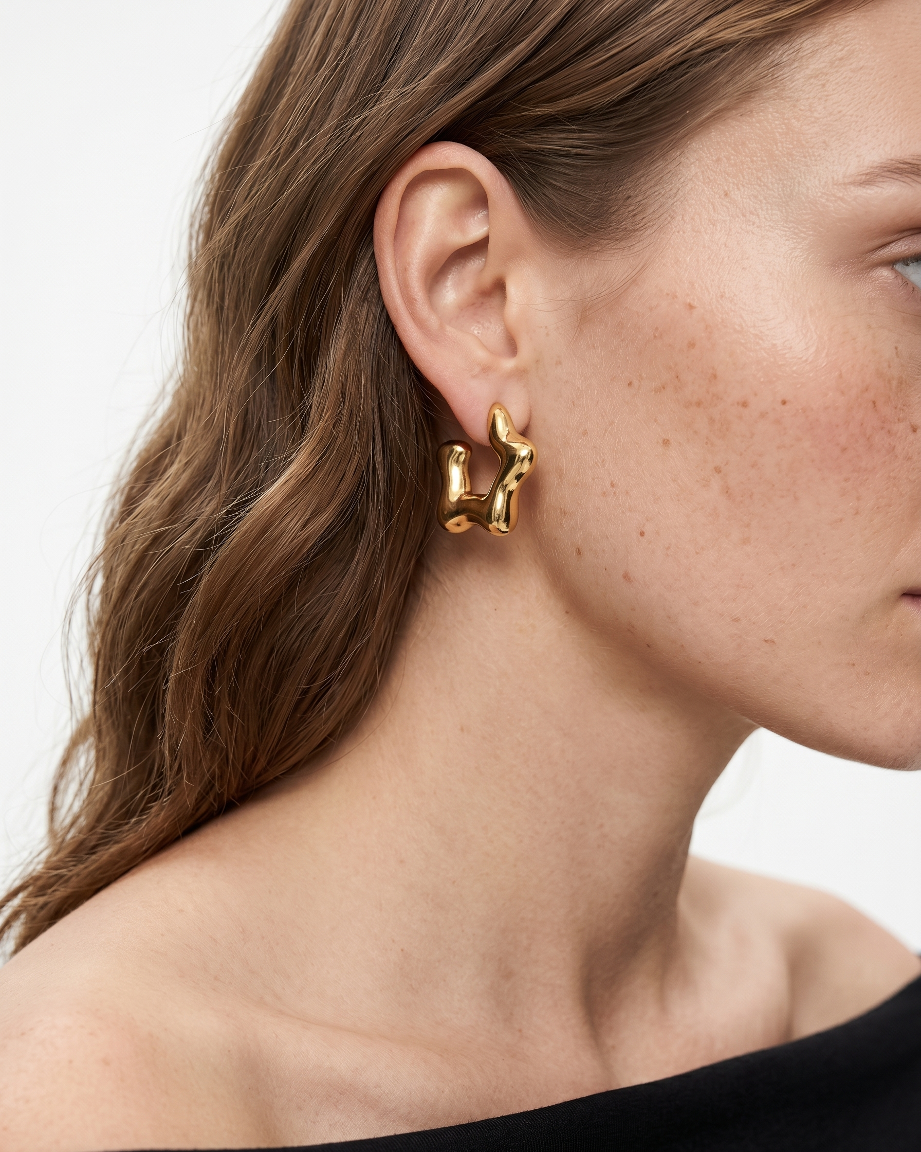 Close-up of a person wearing a gold earring with a white background