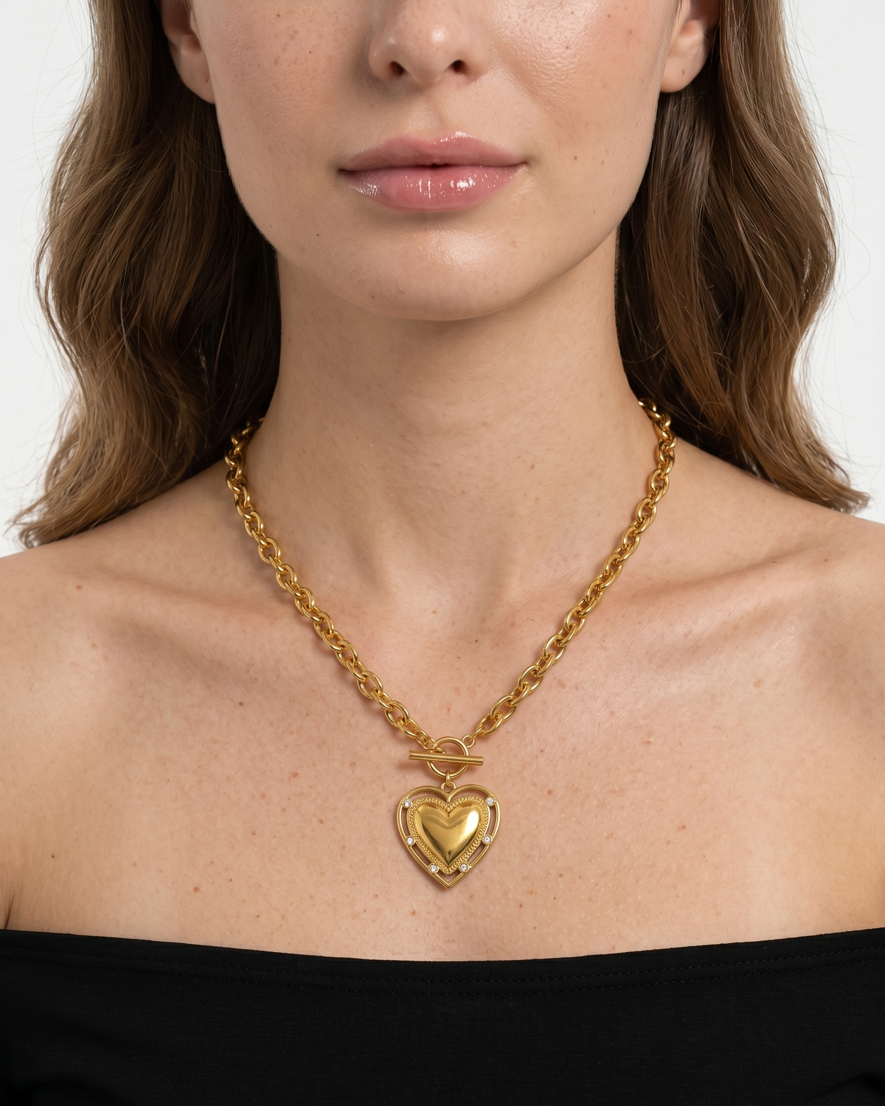 Woman wearing a gold necklace with a heart pendant on a plain background