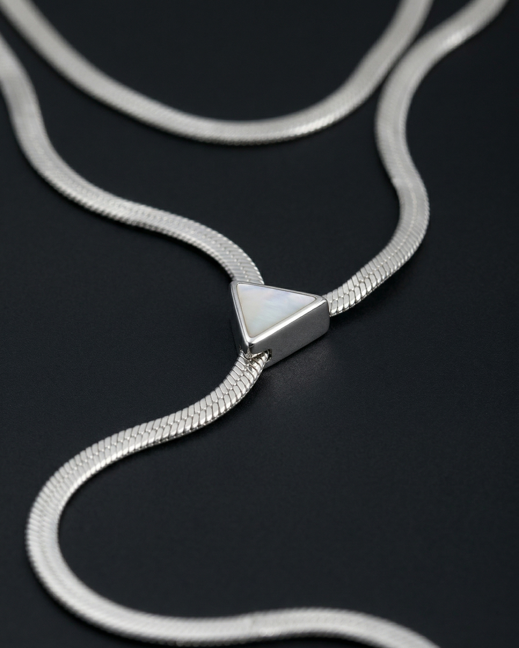 Silver snake chain necklace with a triangular clasp on a black background