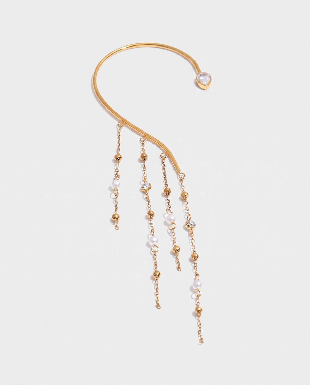 A gold-toned ear cuff earring featuring a curved main bar, a small heart-shaped pearl at the end, and three dangling chains with gold beads and clear faceted pearls, shown on a light gray background.