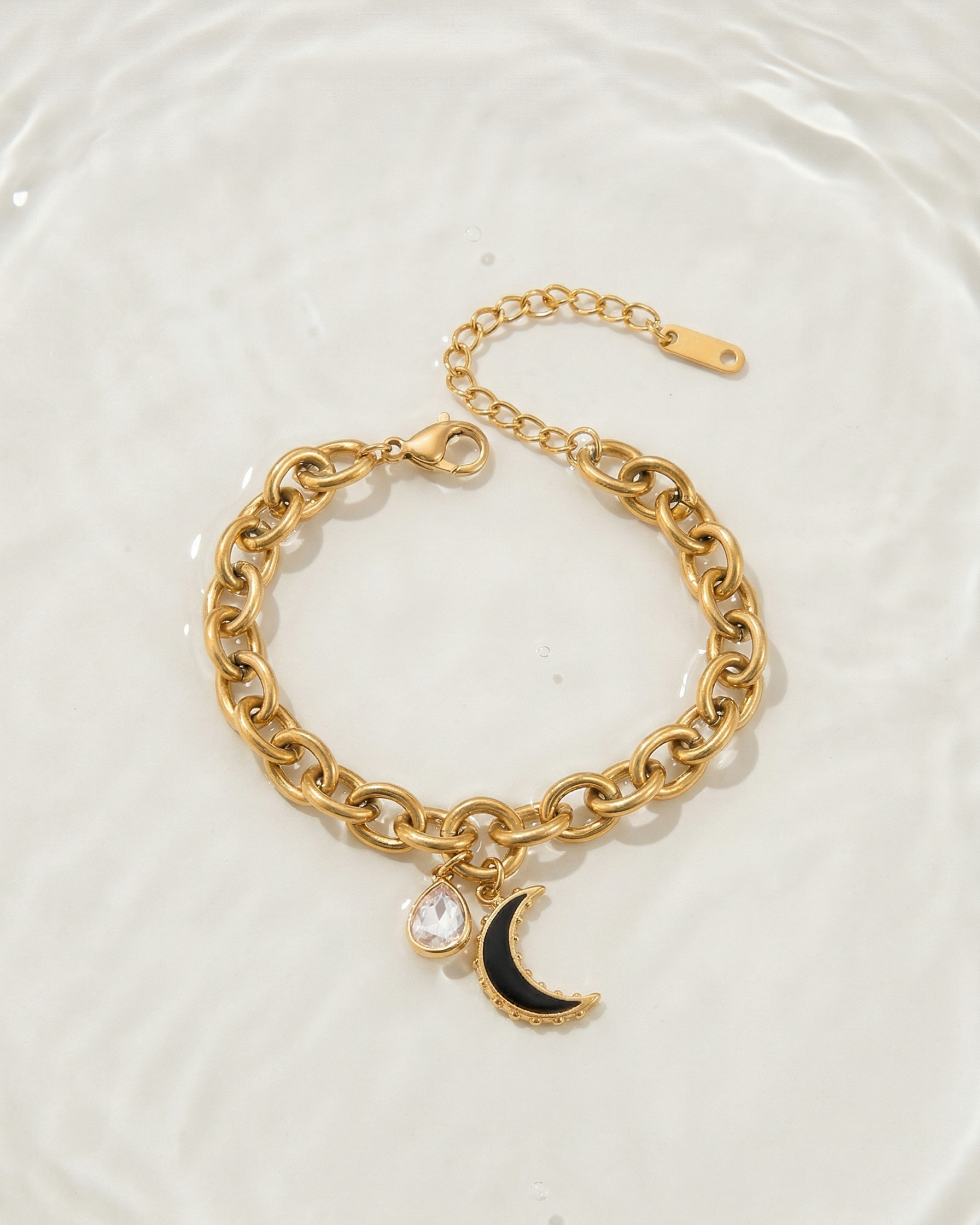 Gold chain bracelet with a moon charm on a white plate
