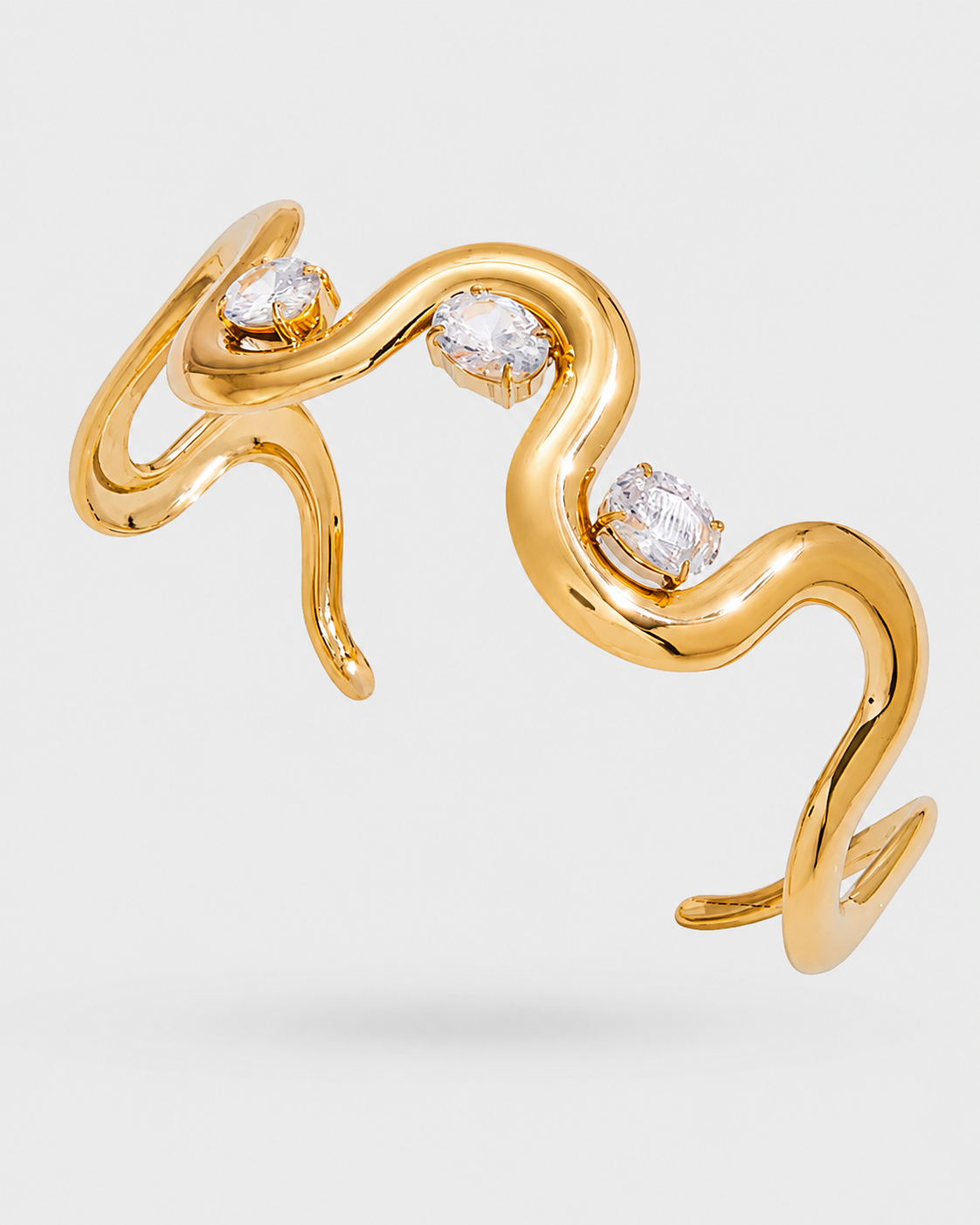 A gold snake-shaped cuff ring with three bezel-set clear round diamonds, shown on a light gray background.