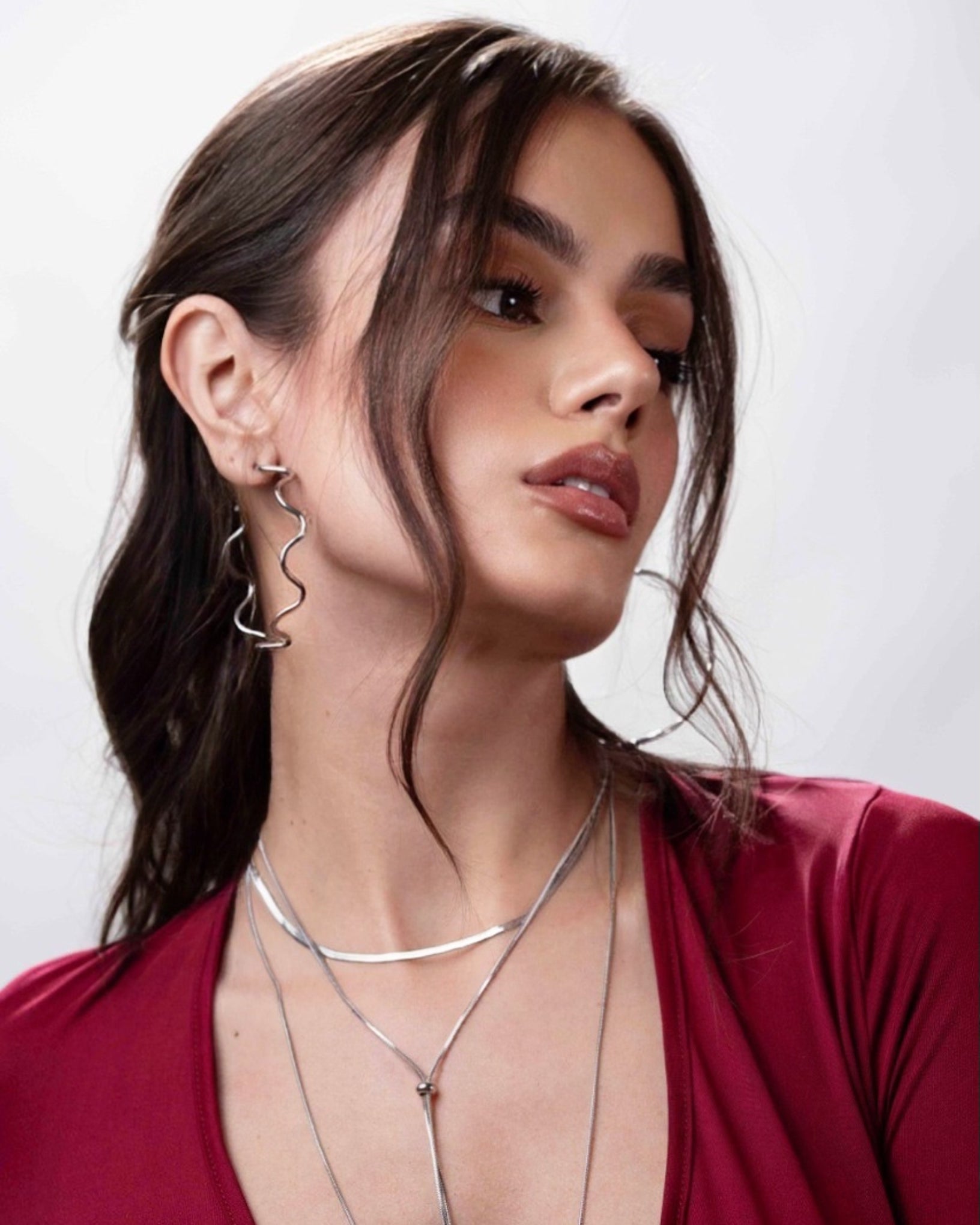 Woman wearing hoop earrings and layered necklaces against a plain background