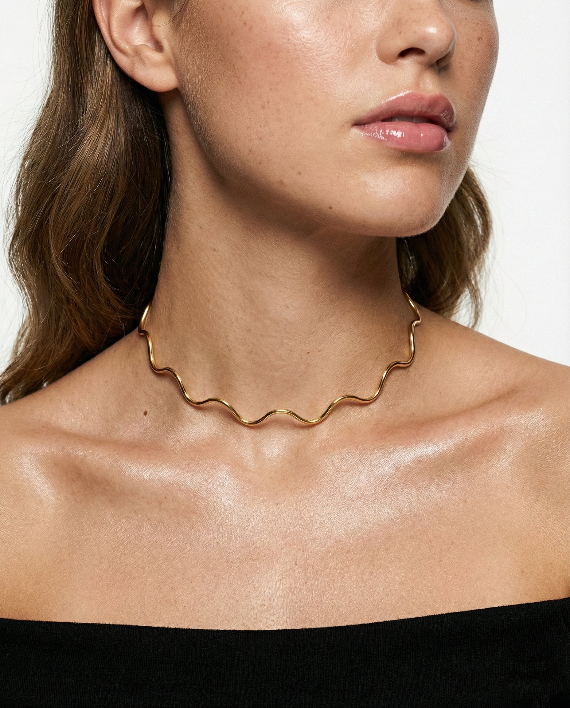 Gold necklace worn by a person on a plain background