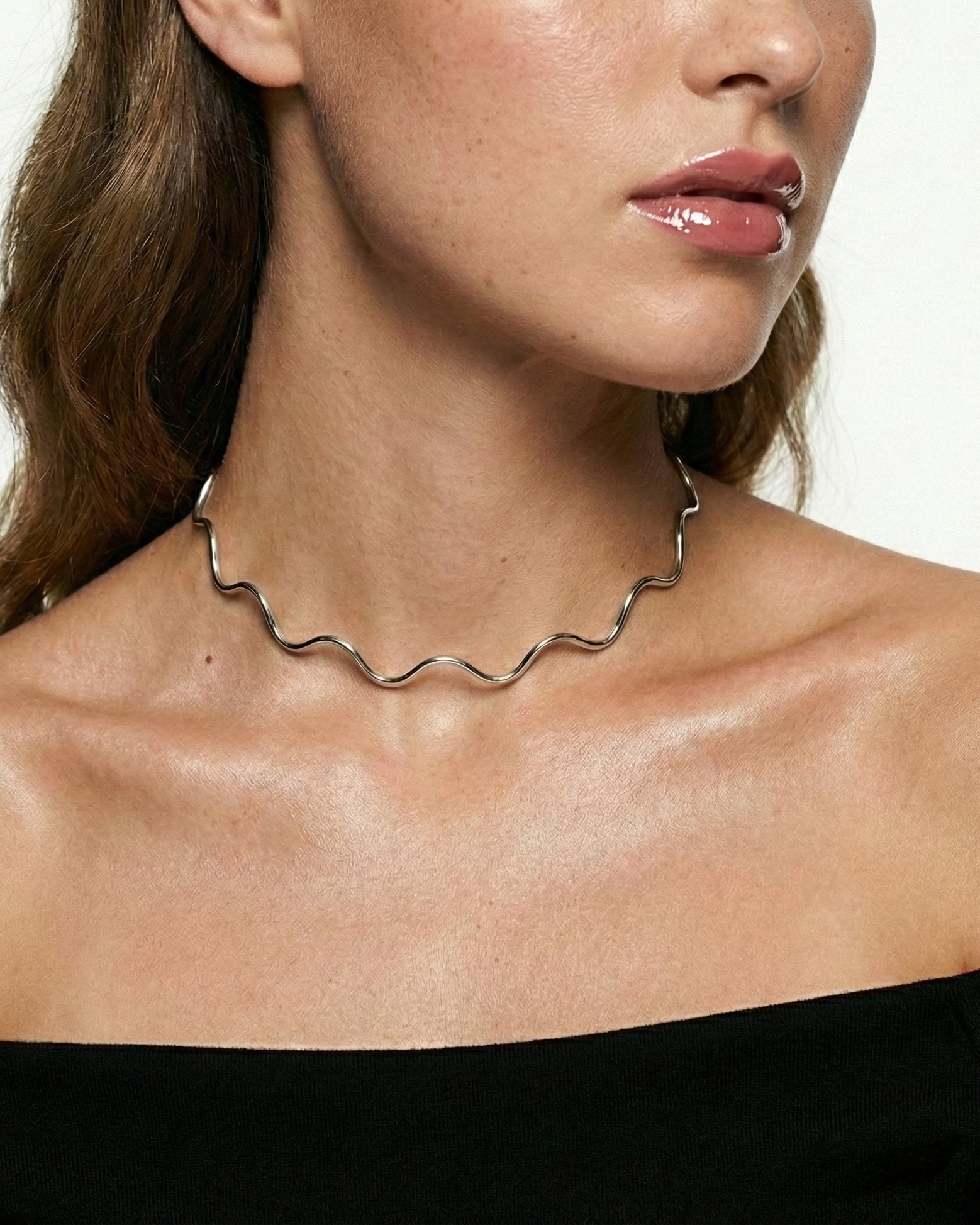 Silver necklace worn by a person against a neutral background