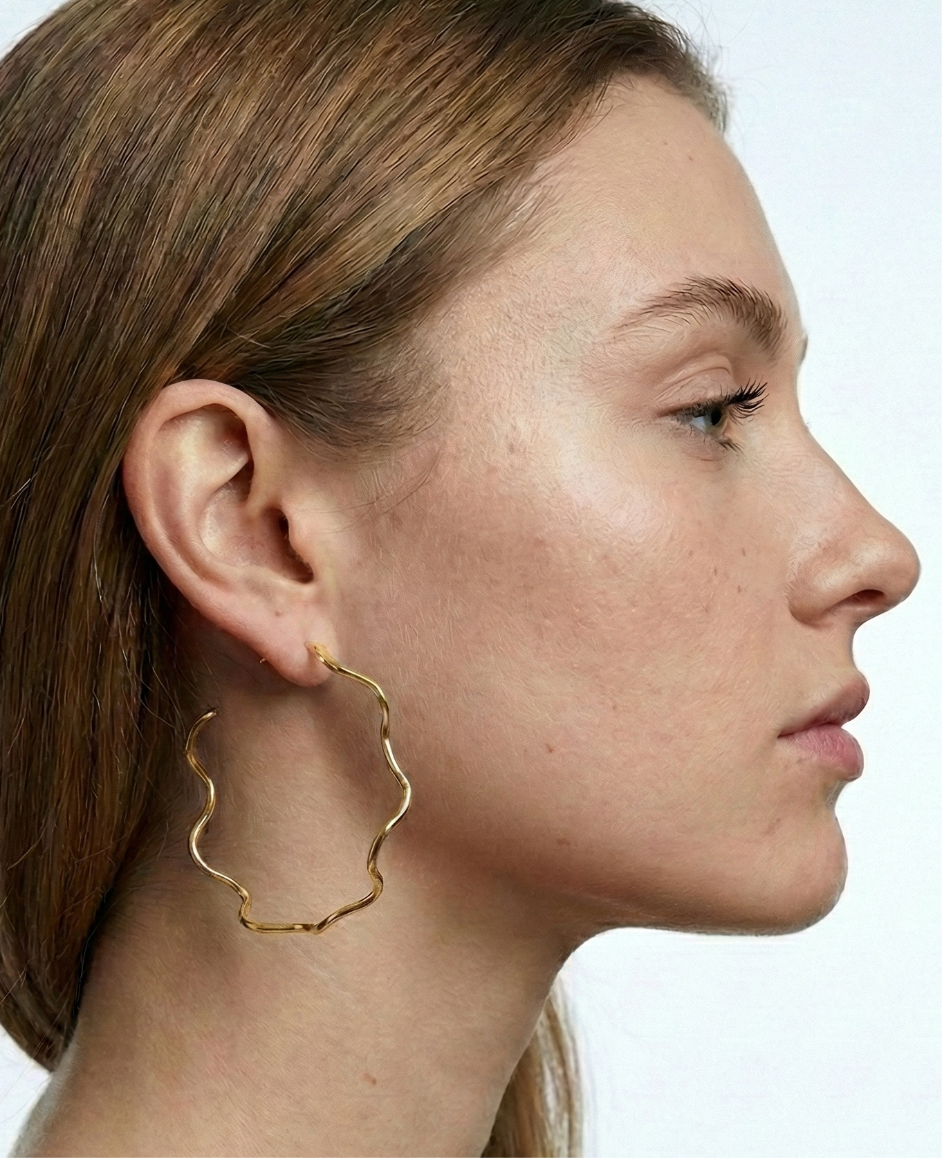 Woman wearing gold hoop earrings with a plain background
