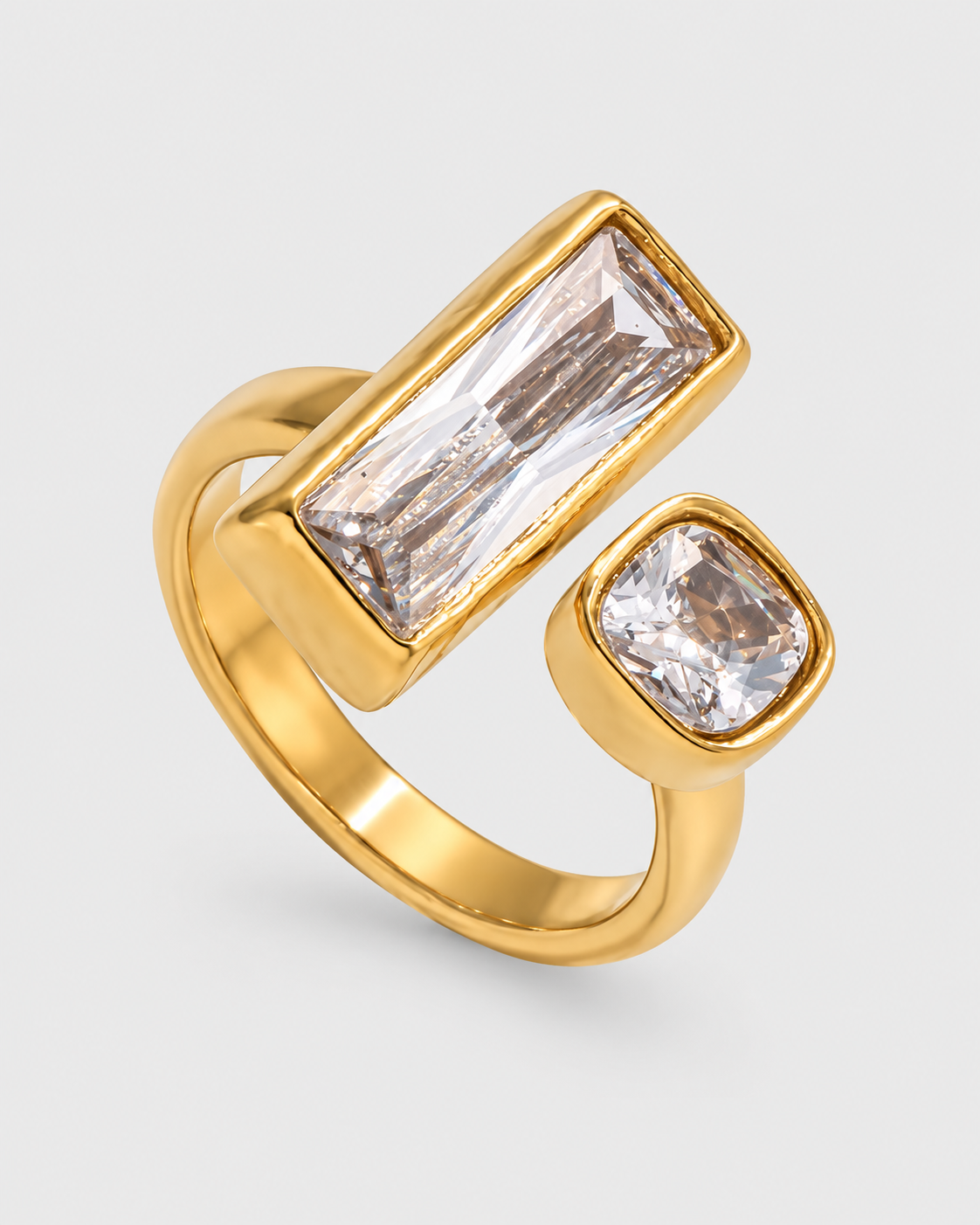 A gold ring featuring two clear rectangular and square-cut gemstones in bezel settings, shown on a light gray background.