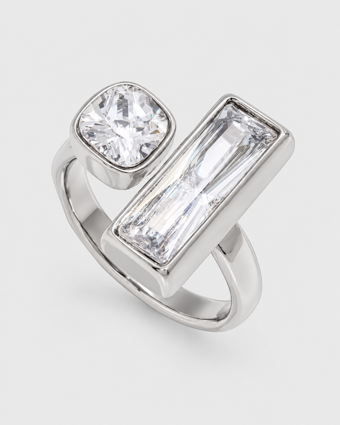 A silver-toned ring featuring a large rectangular baguette-cut clear gemstone and a smaller cushion-cut clear gemstone, photographed on a light gray background.