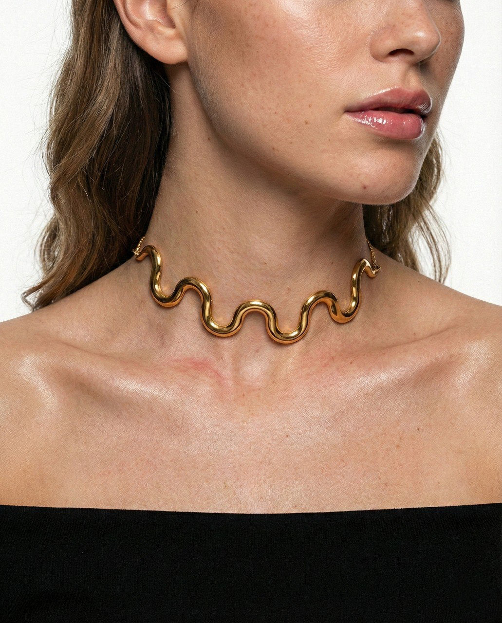Gold wavy necklace worn by a model on a white background