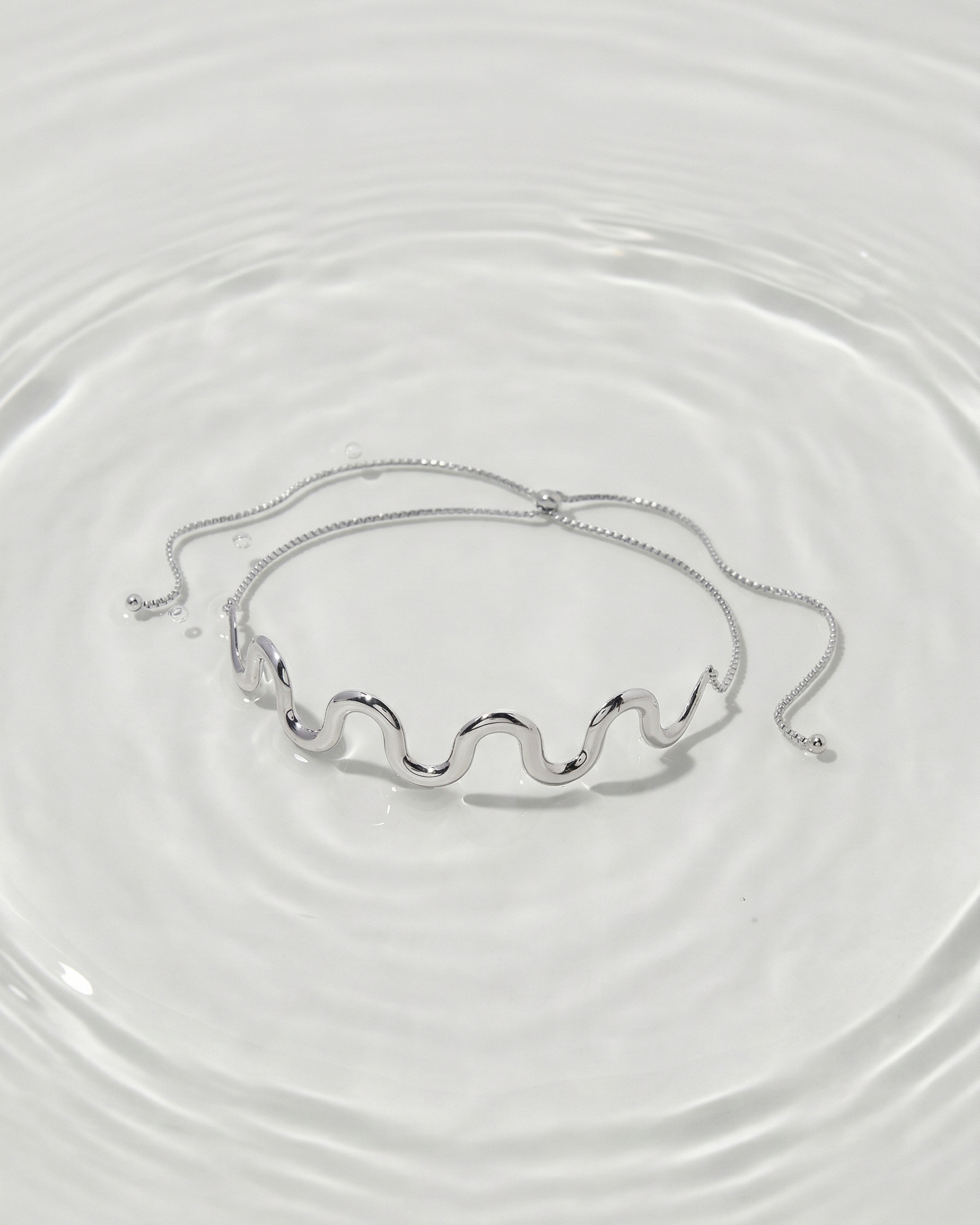 Silver bracelet on a clear glass surface with water ripples