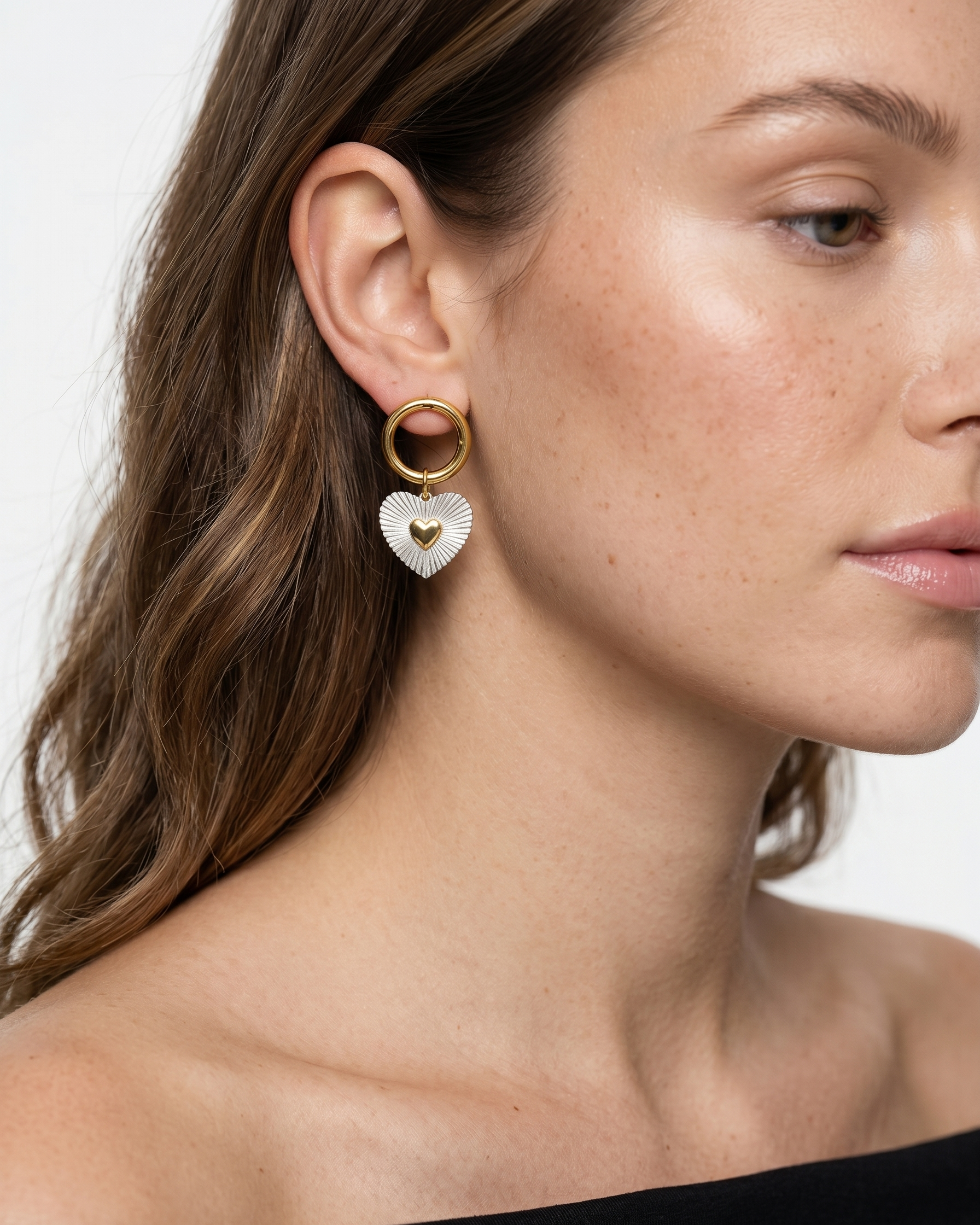 Close-up of a woman wearing gold heart-shaped earrings against a neutral background