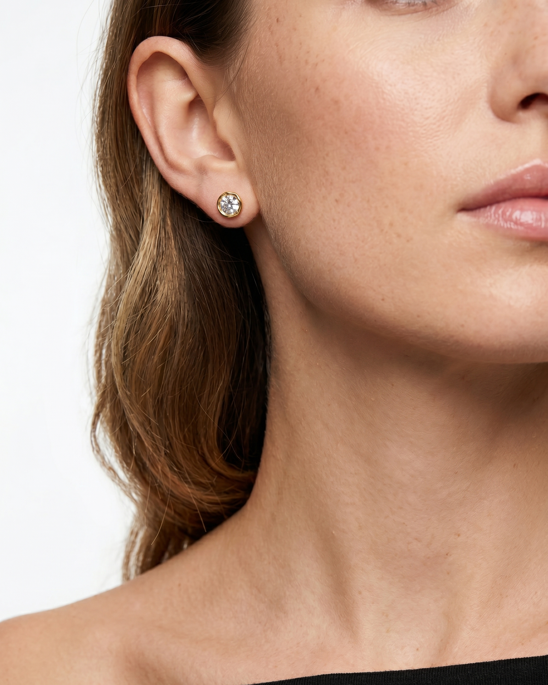 Close-up of a woman wearing diamond stud earrings with a plain background