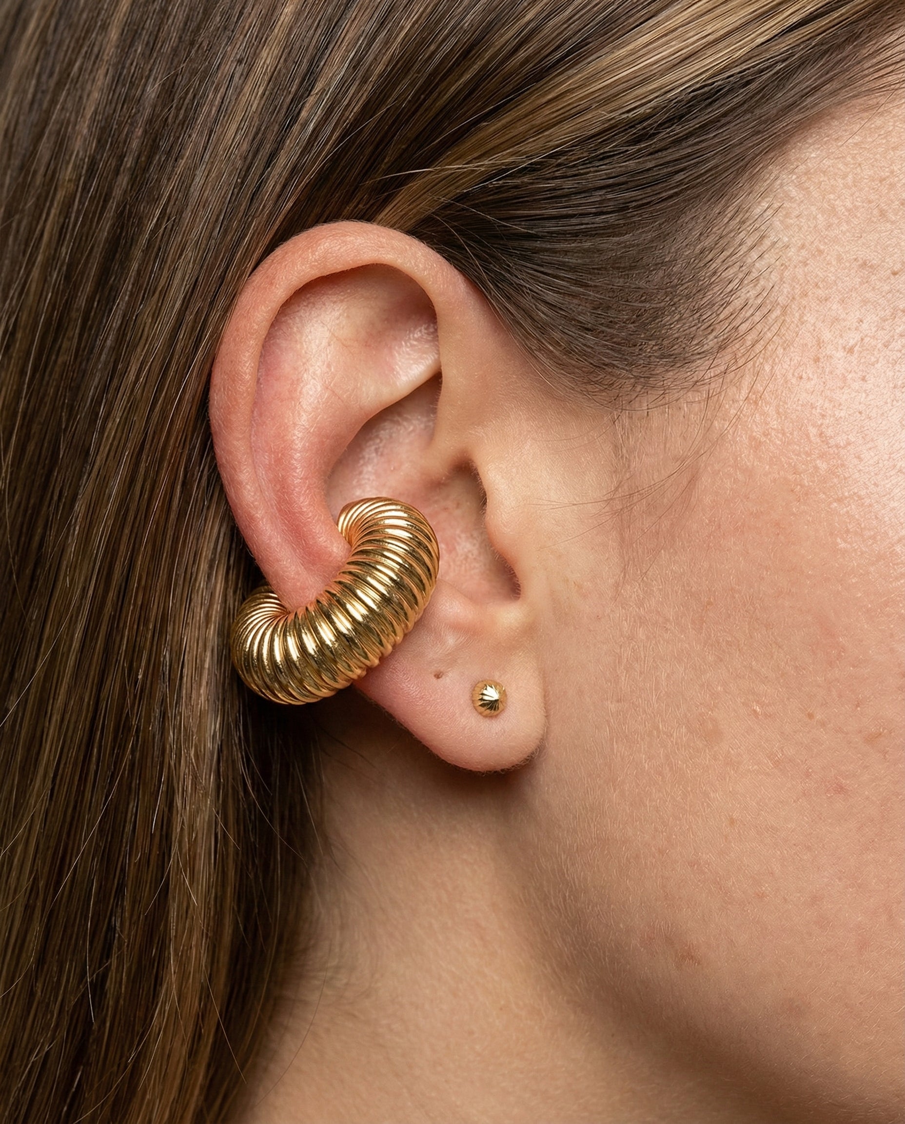 Close-up of an ear wearing a gold spiral earring with another small earring.