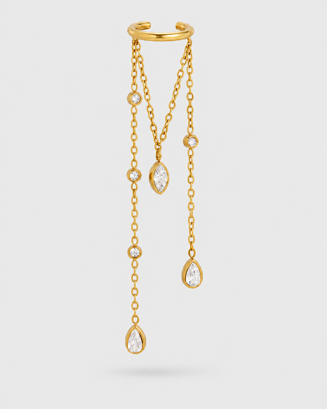 A gold-toned dangle earring with a curved top band, three hanging chains, and clear teardrop and round gemstones on a light gray background.