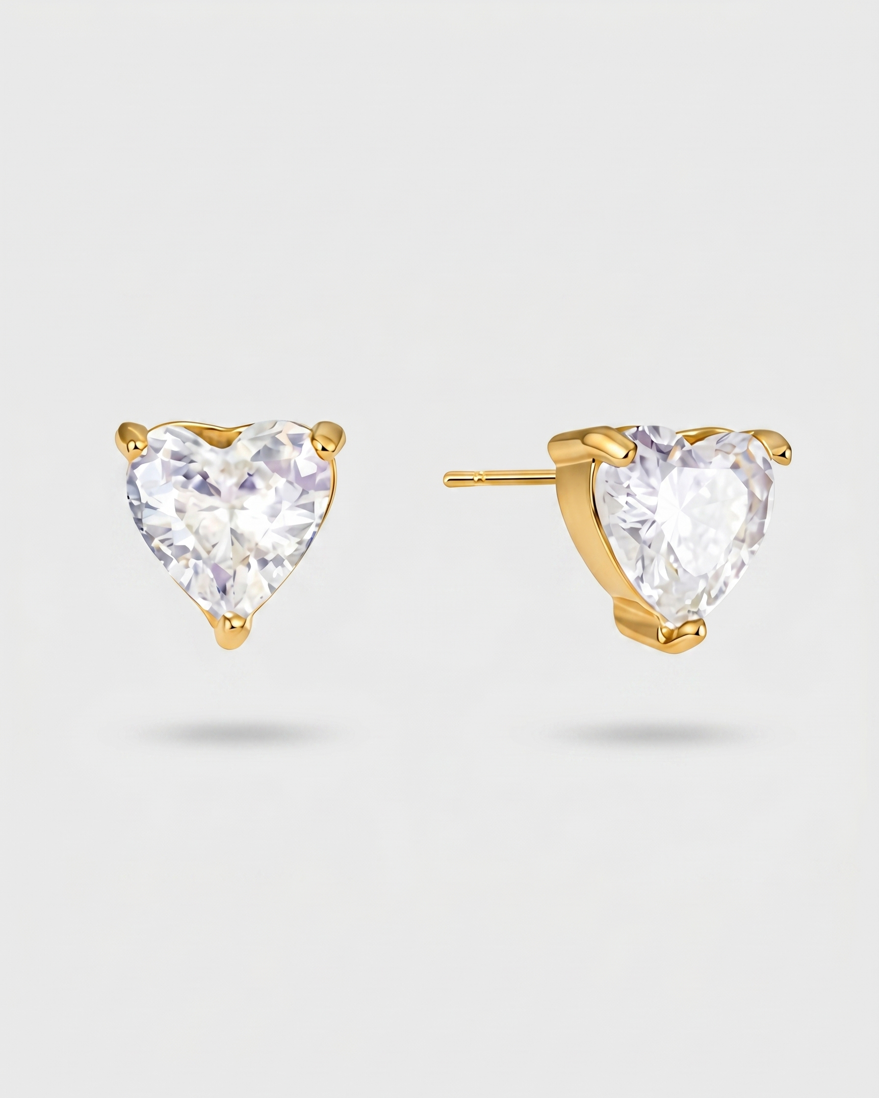 Gold heart-shaped stud earrings with clear gemstones on a light gray background