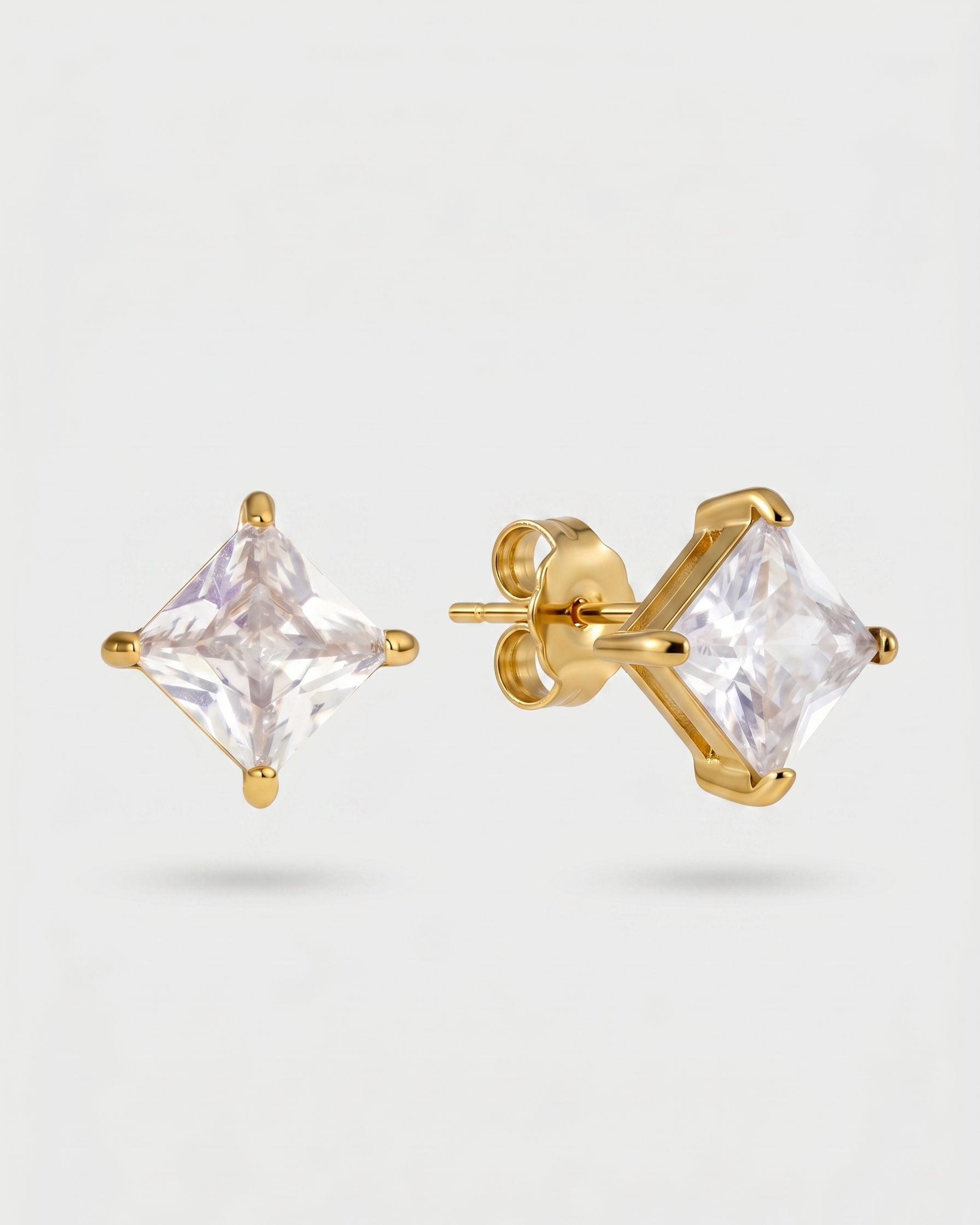 Gold stud earrings with clear gemstones on a light gray background