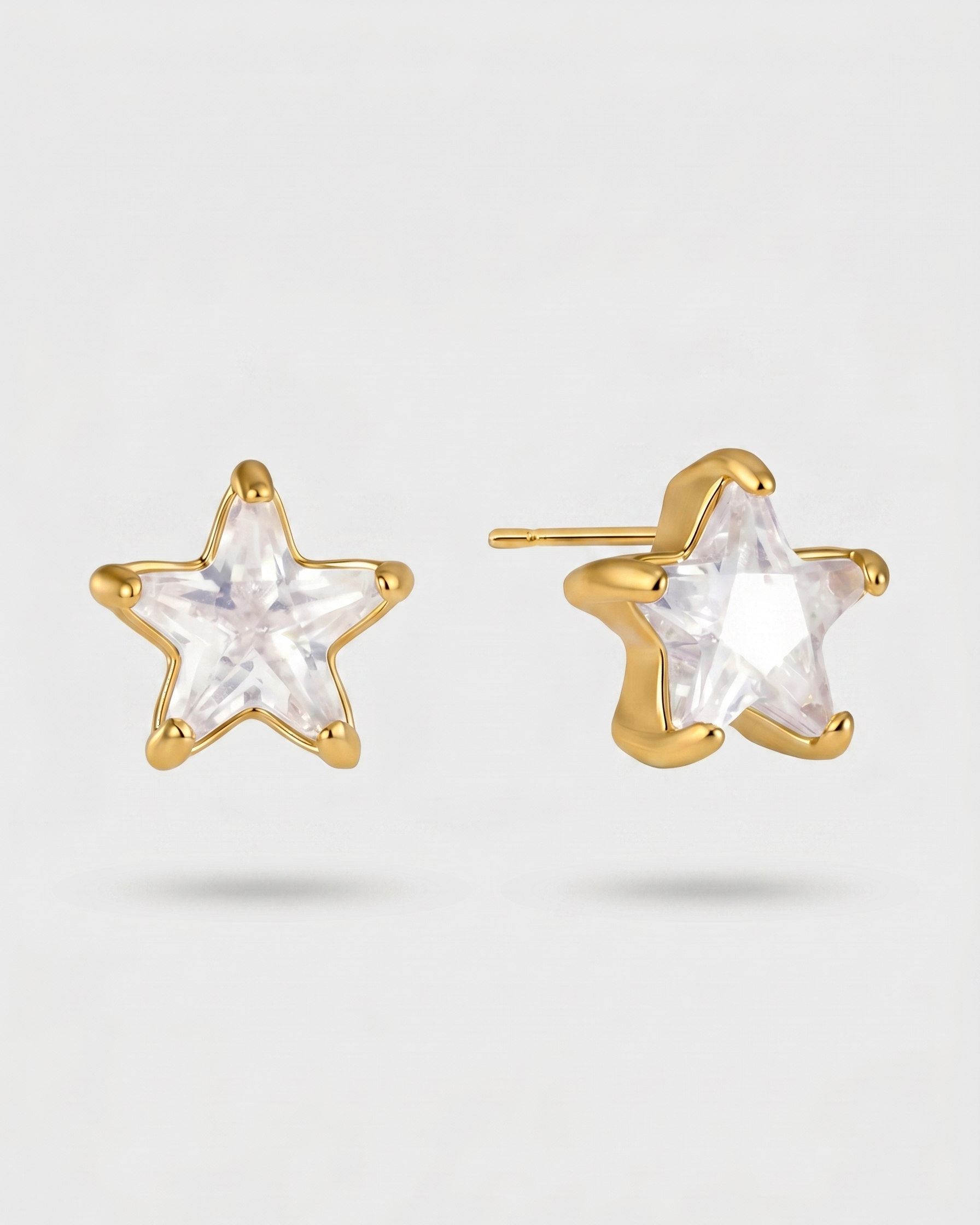 Gold star-shaped earrings with clear gemstones on a light gray background