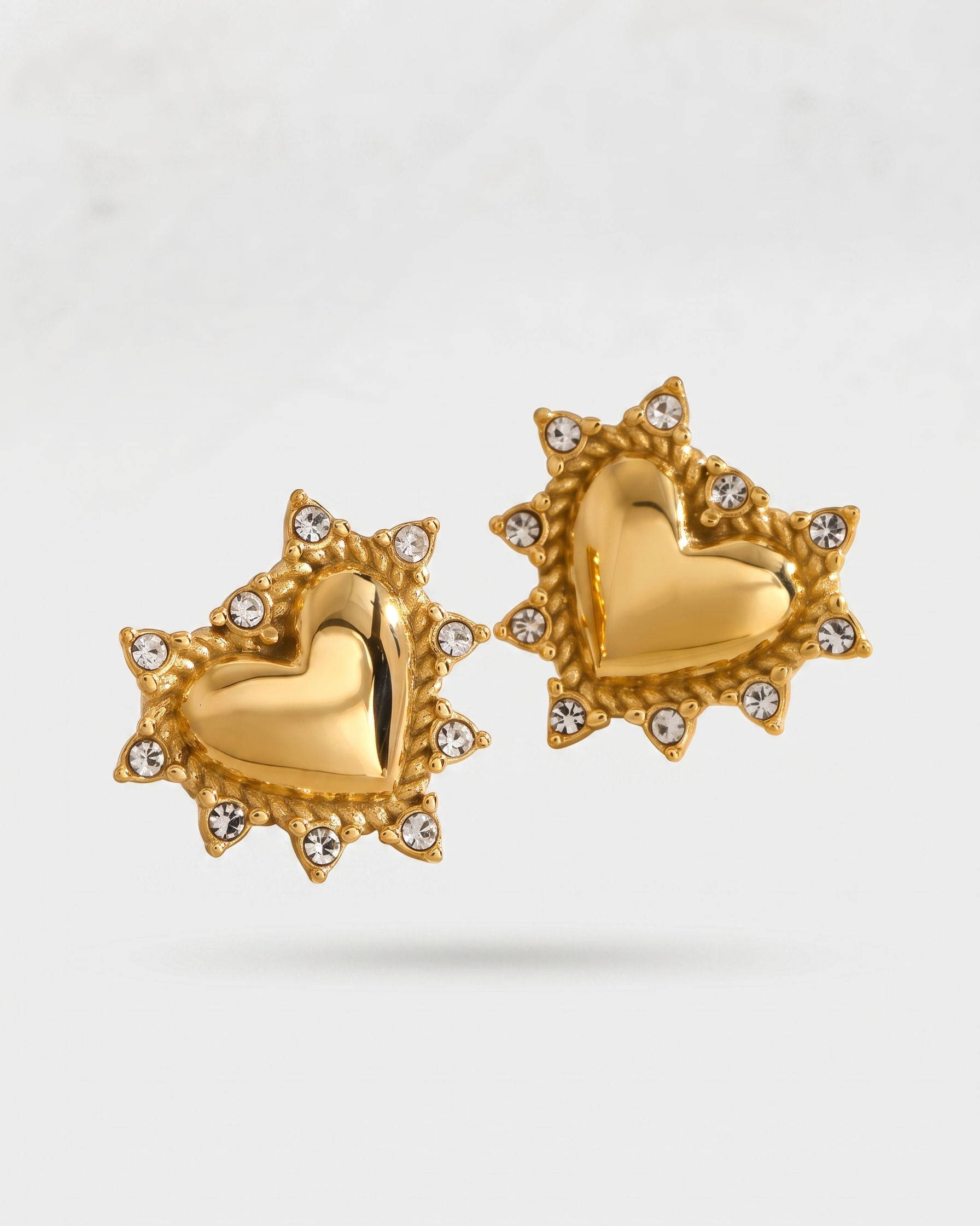 Gold heart-shaped earrings with diamond accents on a light gray background