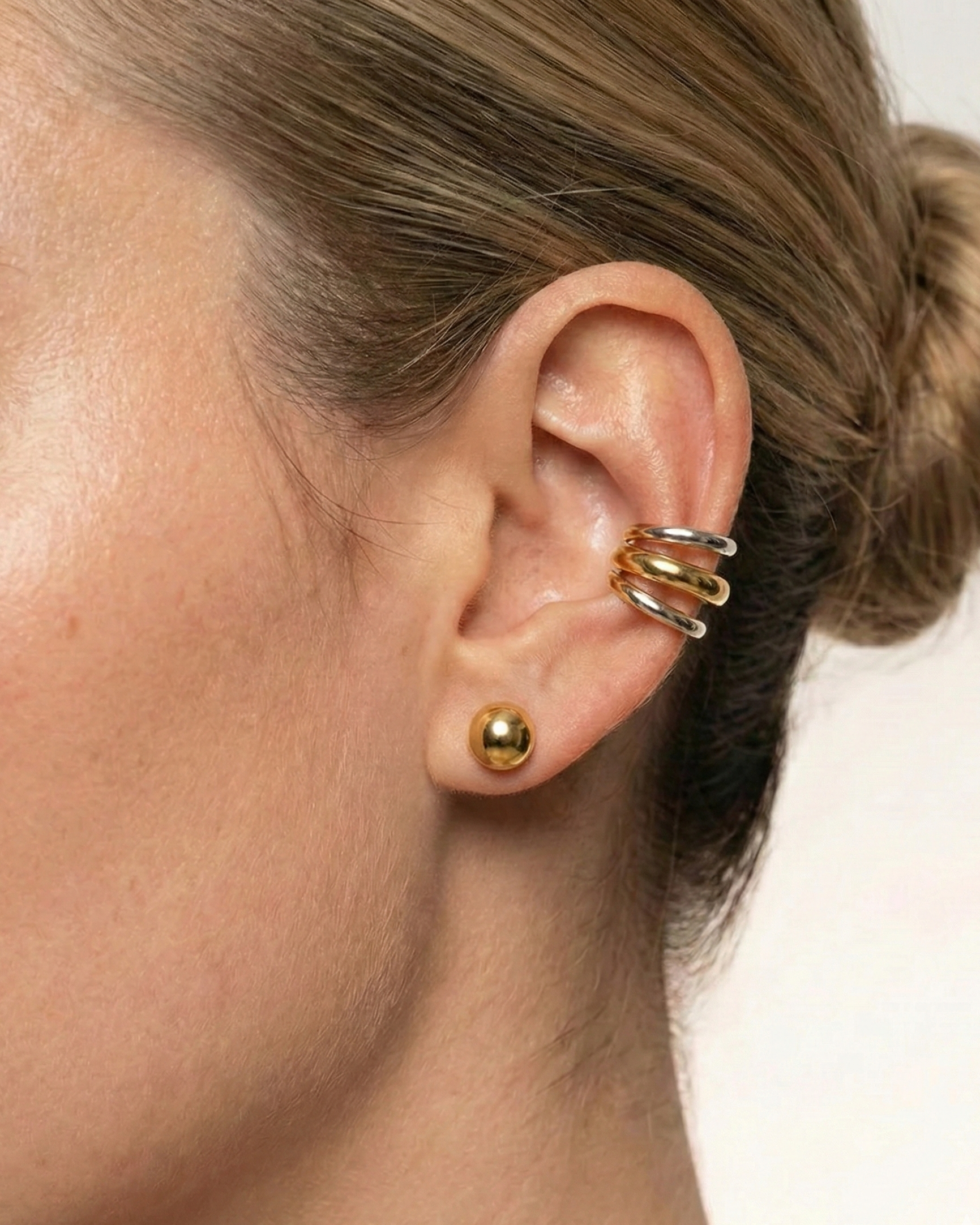 Close-up of an ear with gold earrings on a plain background