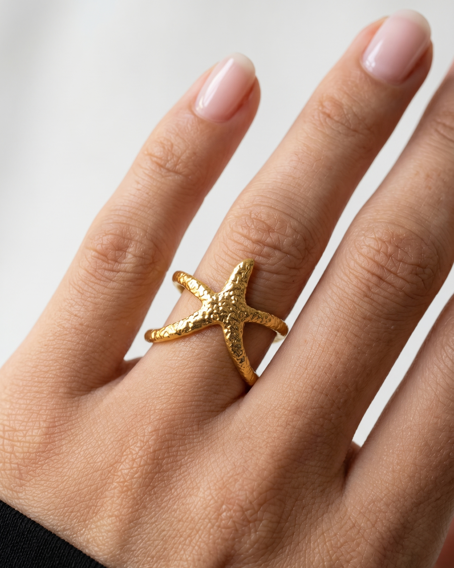 Gold starfish ring on a person's finger against a neutral background