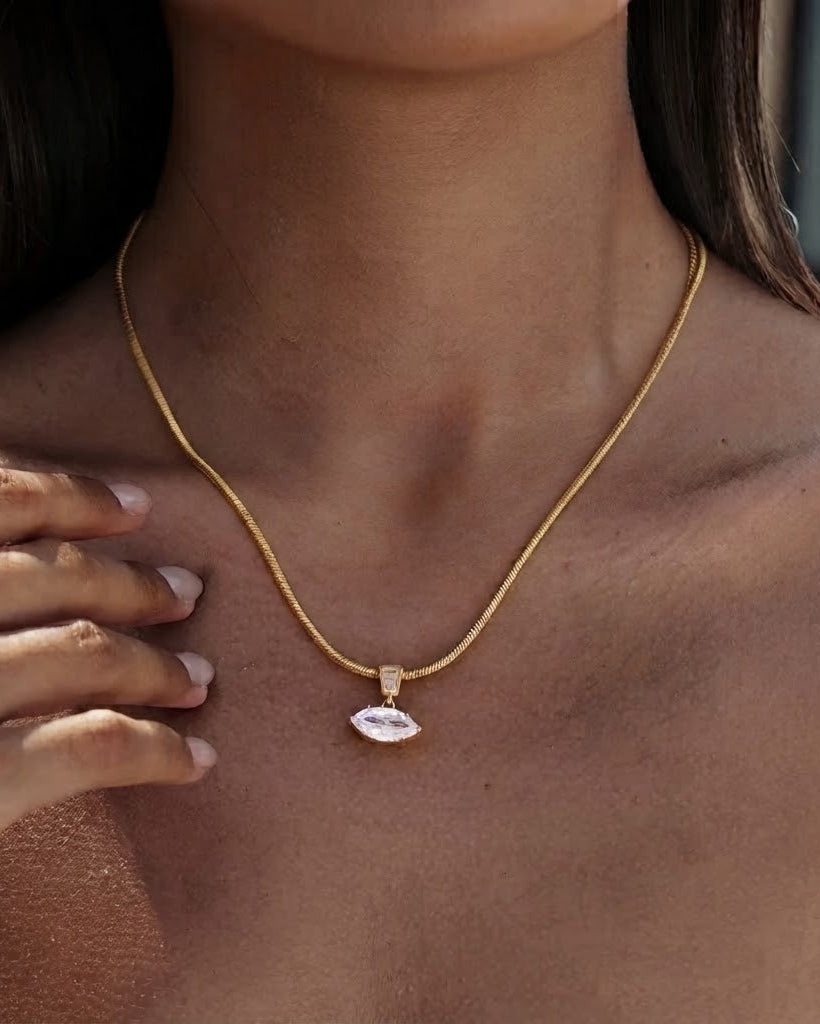 A close-up of a model wearing a delicate gold chain necklace with a small, polished white stone pendant.