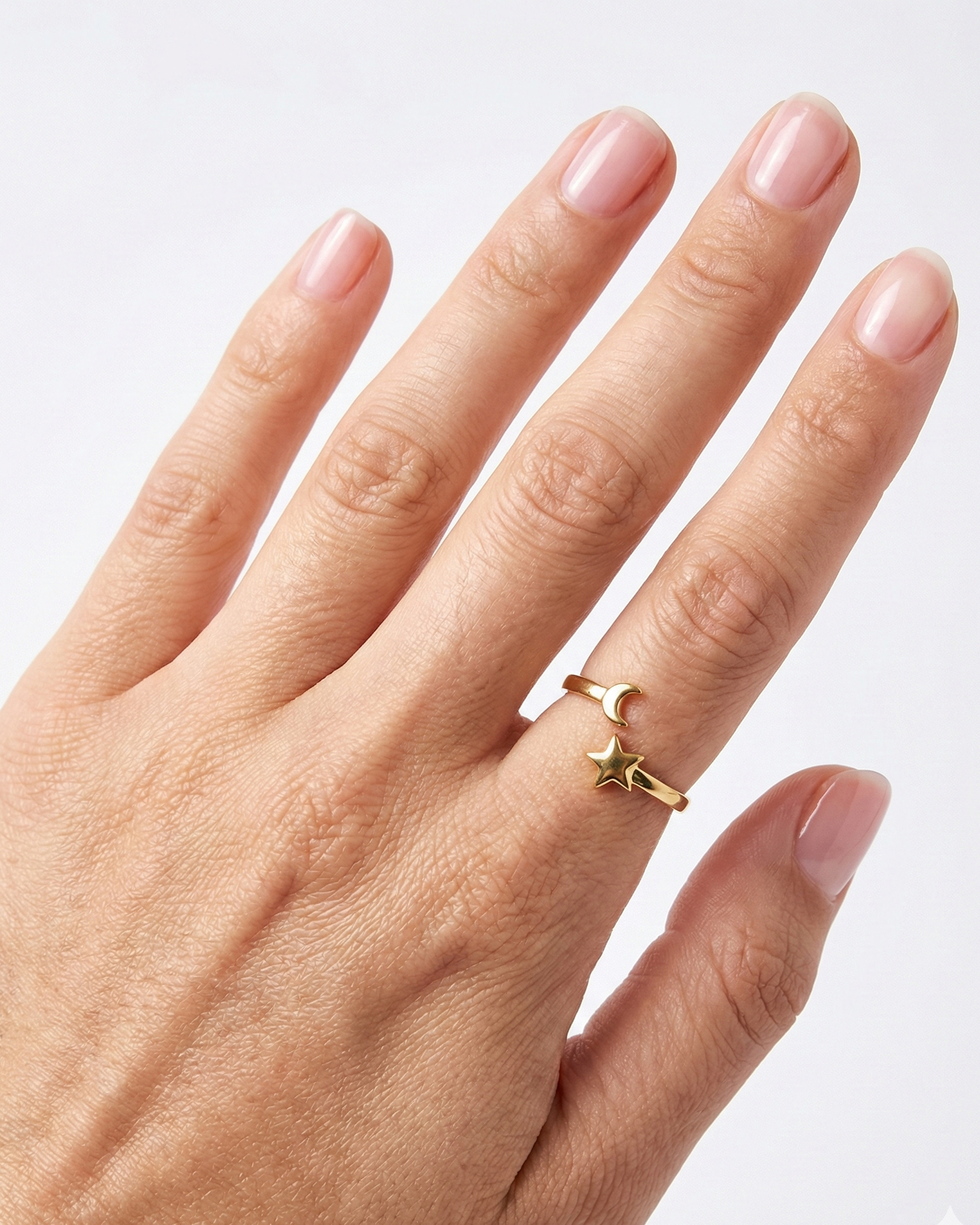 Hand wearing a gold ring with a star design on a light background