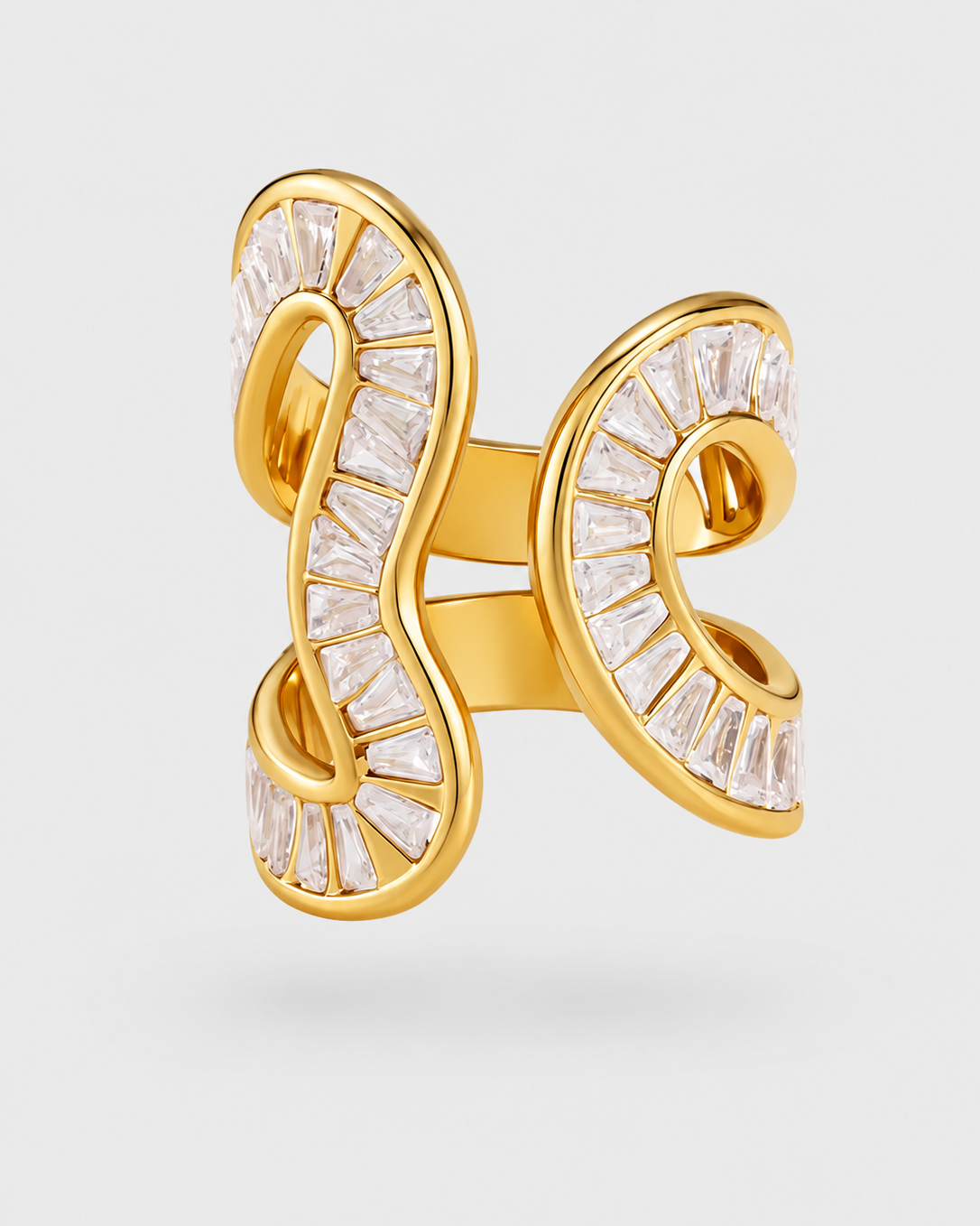 Gold ring with a sculptural, open interlocking design, paved with clear baguette-cut stones, shown on a light gray background.