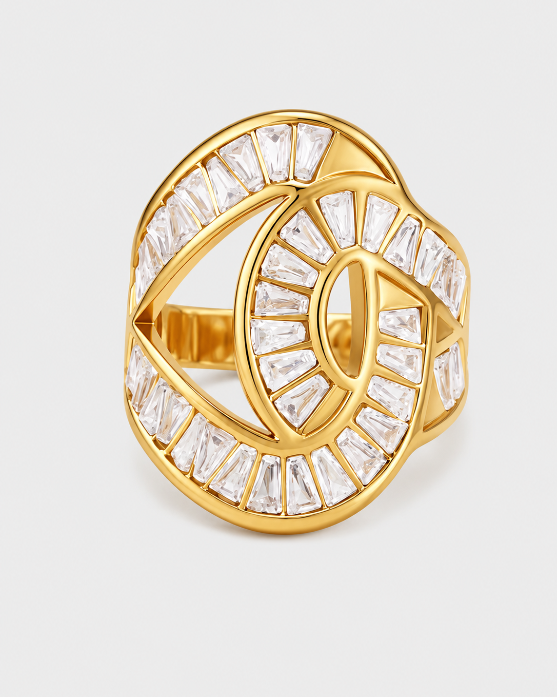 A gold ring featuring an intricate, interlocking circular design paved with clear baguette and round crystals, set against a light gray background.