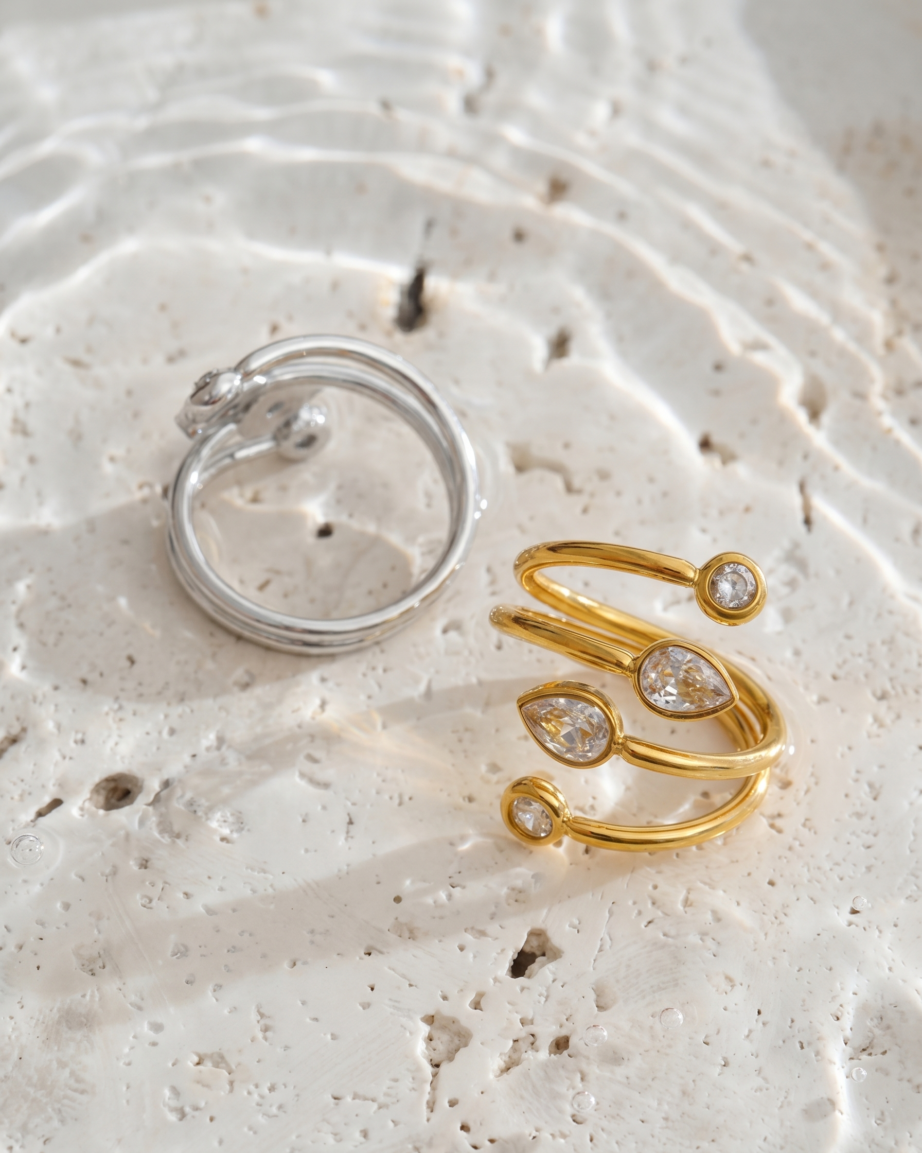 Two rings, one silver and one gold with gemstones, on a textured white surface.