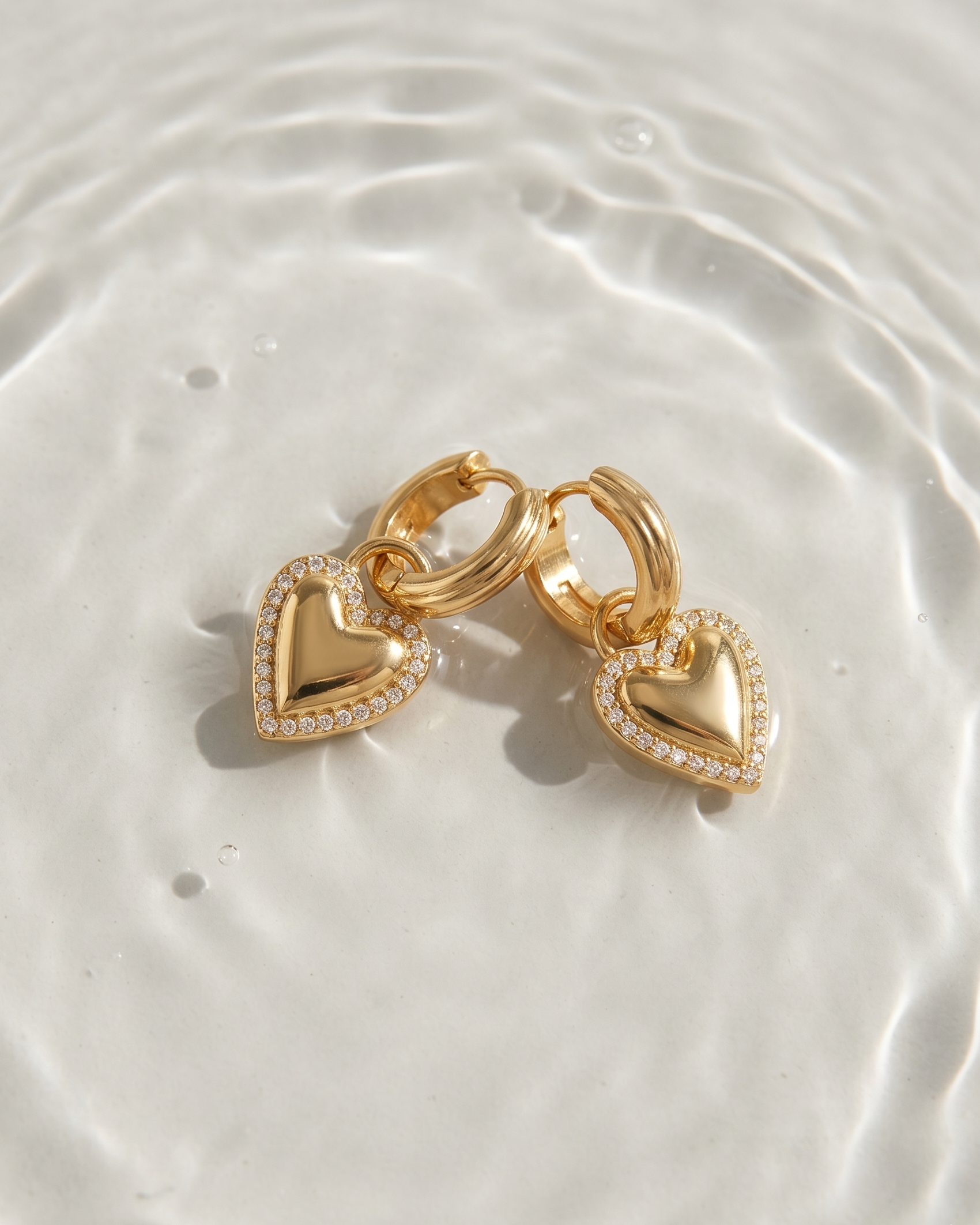 Gold heart-shaped earrings on a textured white surface