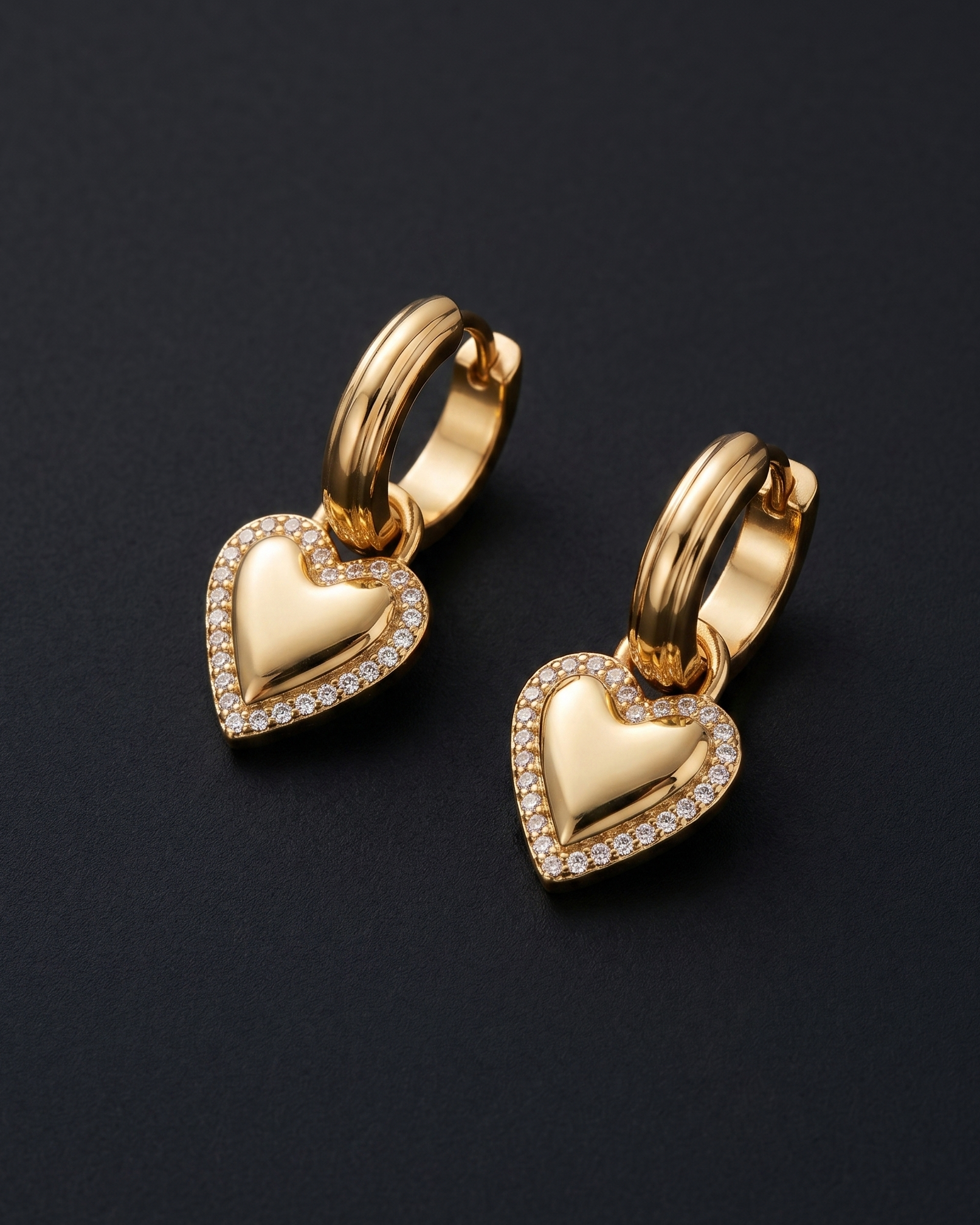 Gold heart-shaped earrings with small diamonds on a black background