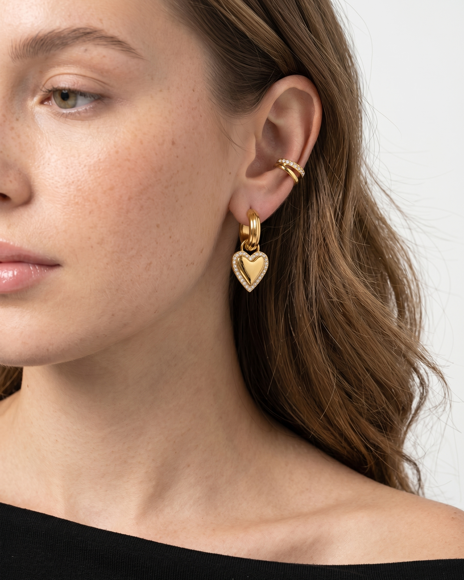 Close-up of a woman wearing gold hoop earrings with heart designs.