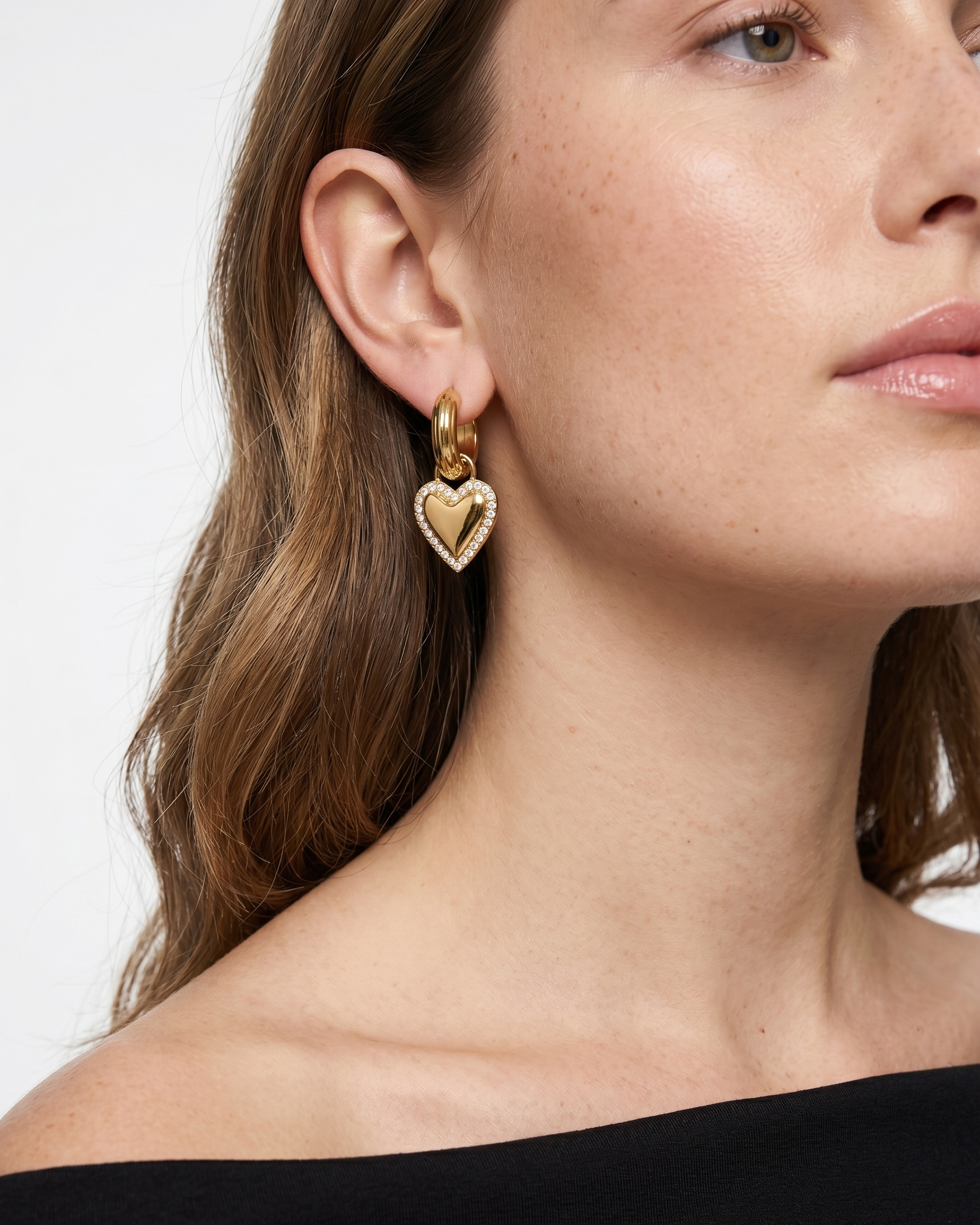 Close-up of a woman wearing gold heart-shaped earrings against a white background