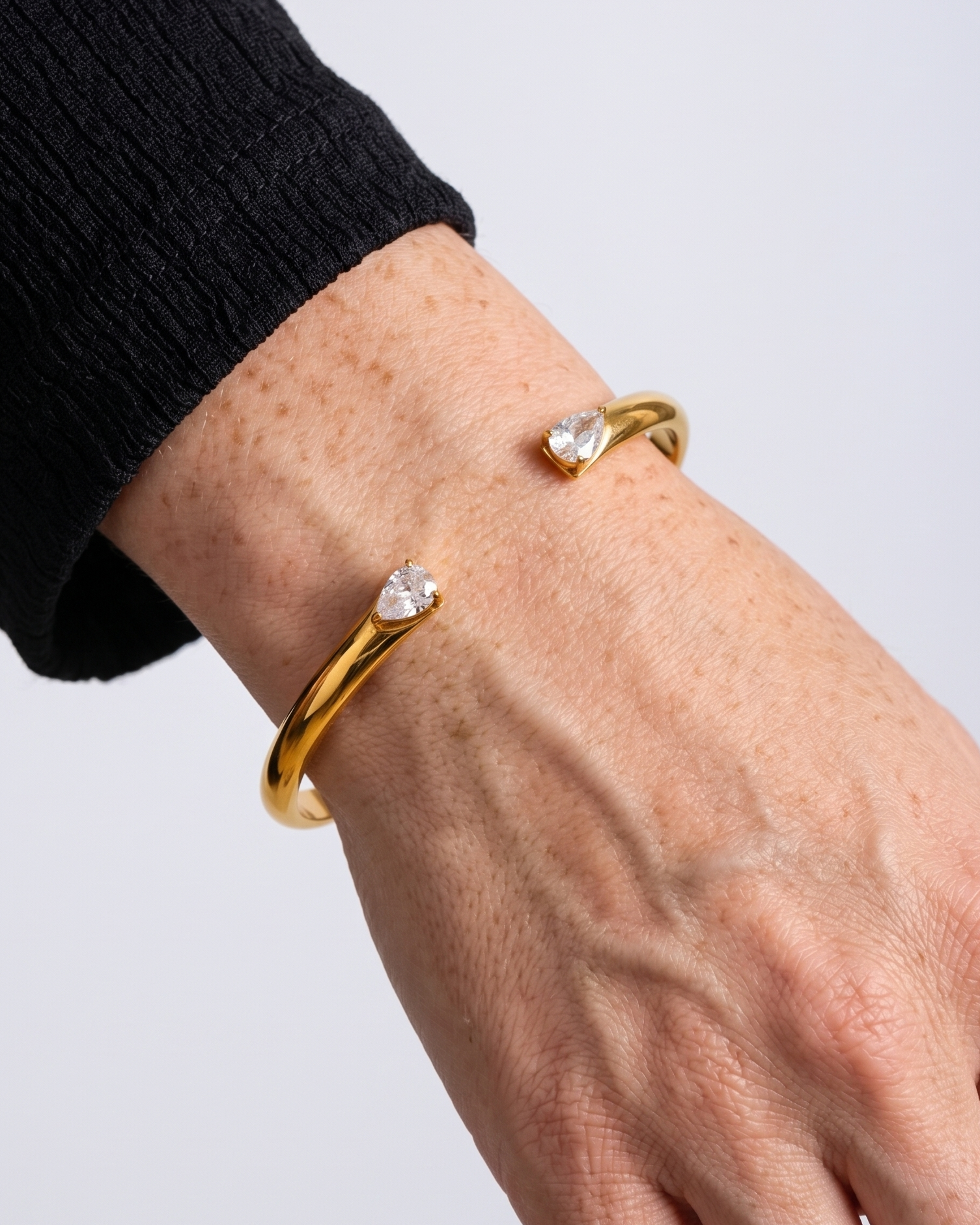 Gold bracelet with heart-shaped stones on a wrist against a light gray background