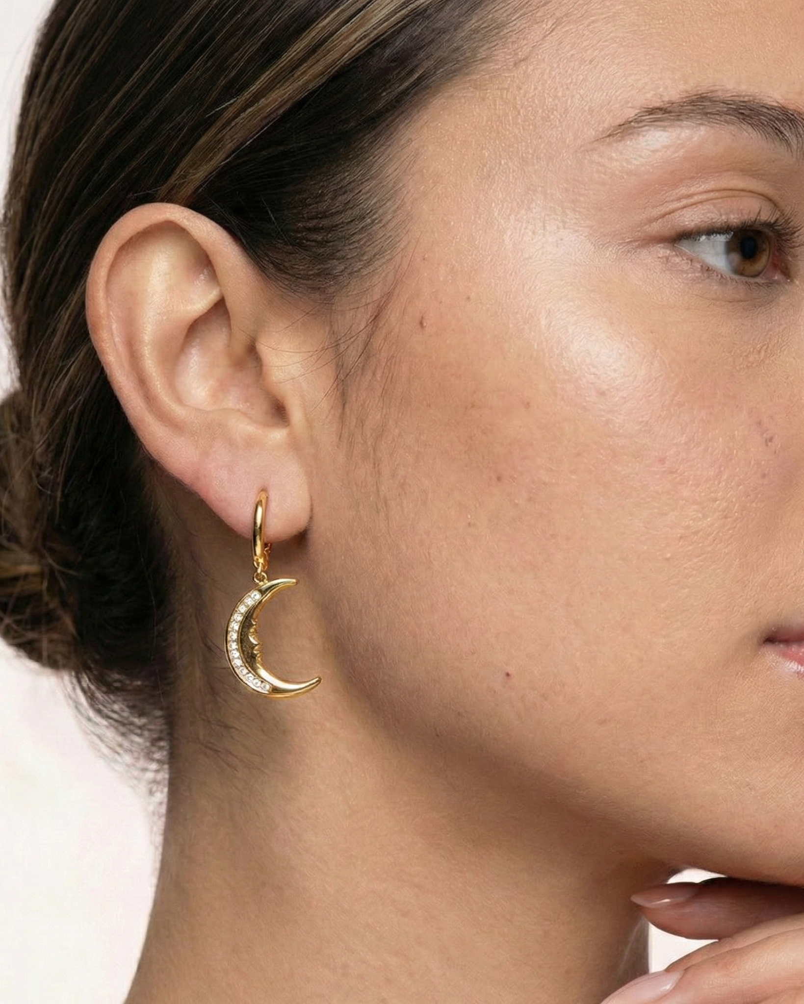 Close-up of a woman wearing a gold hoop earring with a moon design.