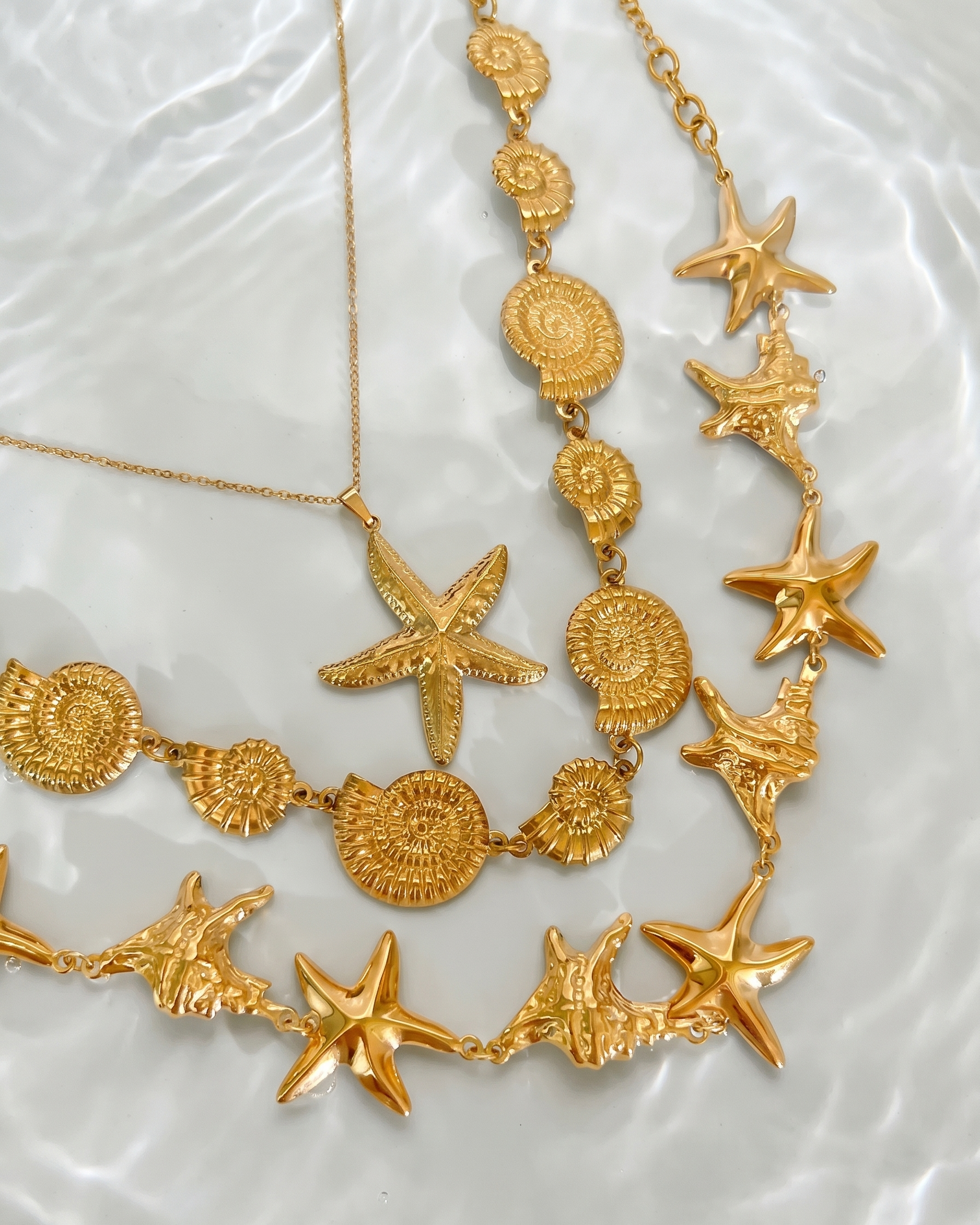 Gold necklace with starfish and circular designs on a textured white surface