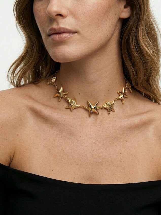Woman wearing a gold star-shaped necklace against a plain background