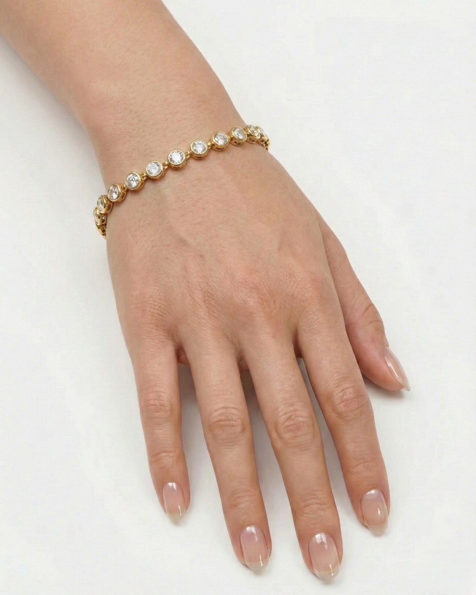 Hand wearing a gold bracelet with clear stones on a white background