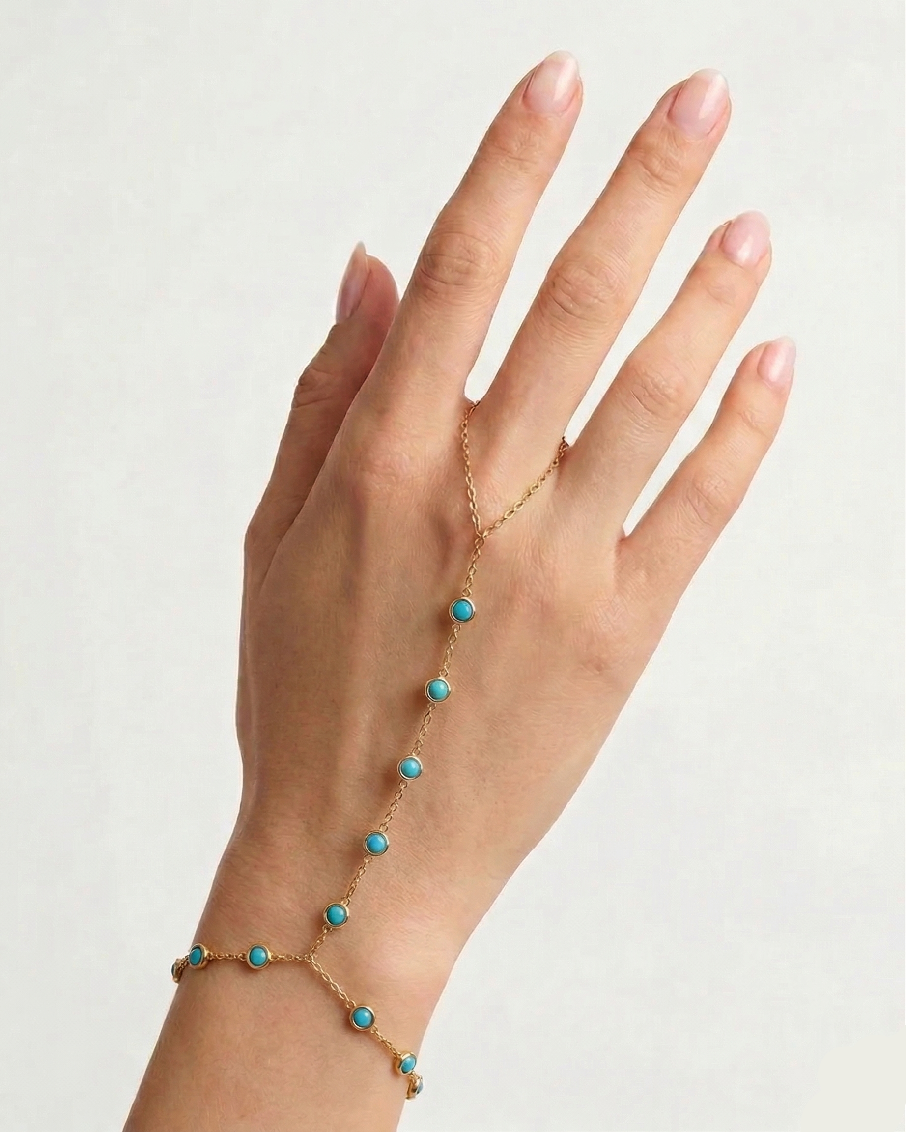 Hand wearing a turquoise beaded bracelet on a plain background