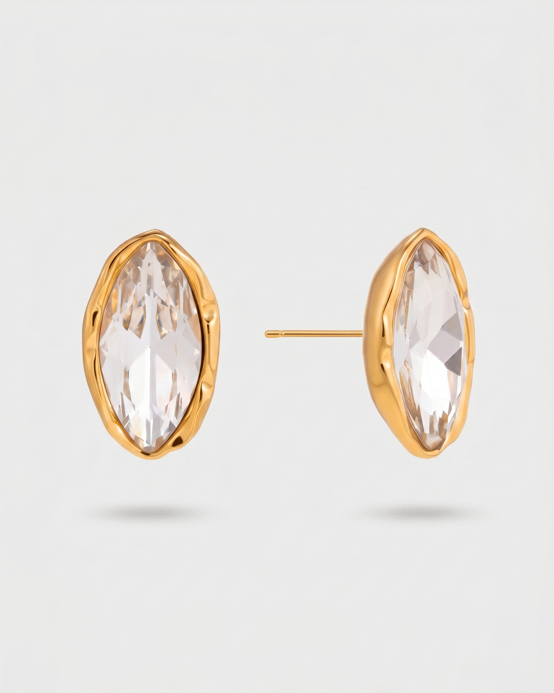 Gold earrings with clear gemstones on a light gray background