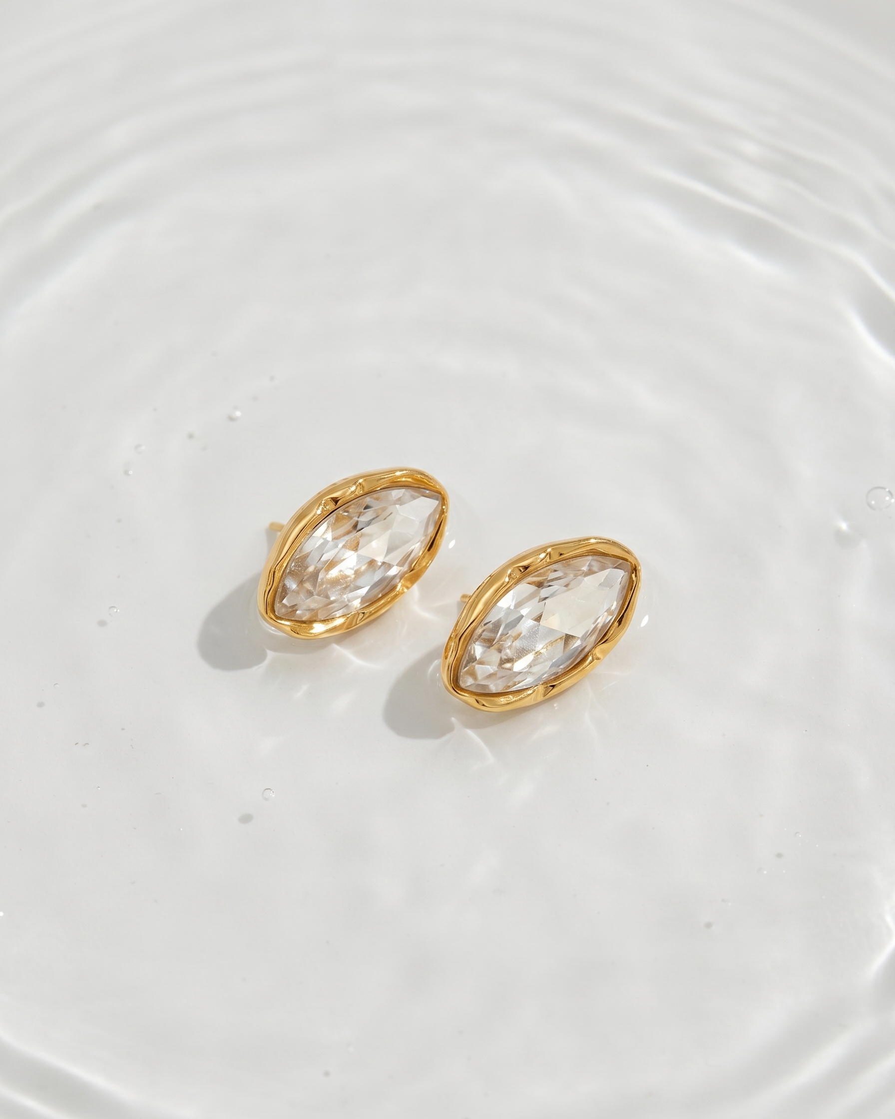 Gold earrings with clear gemstones on a white textured surface