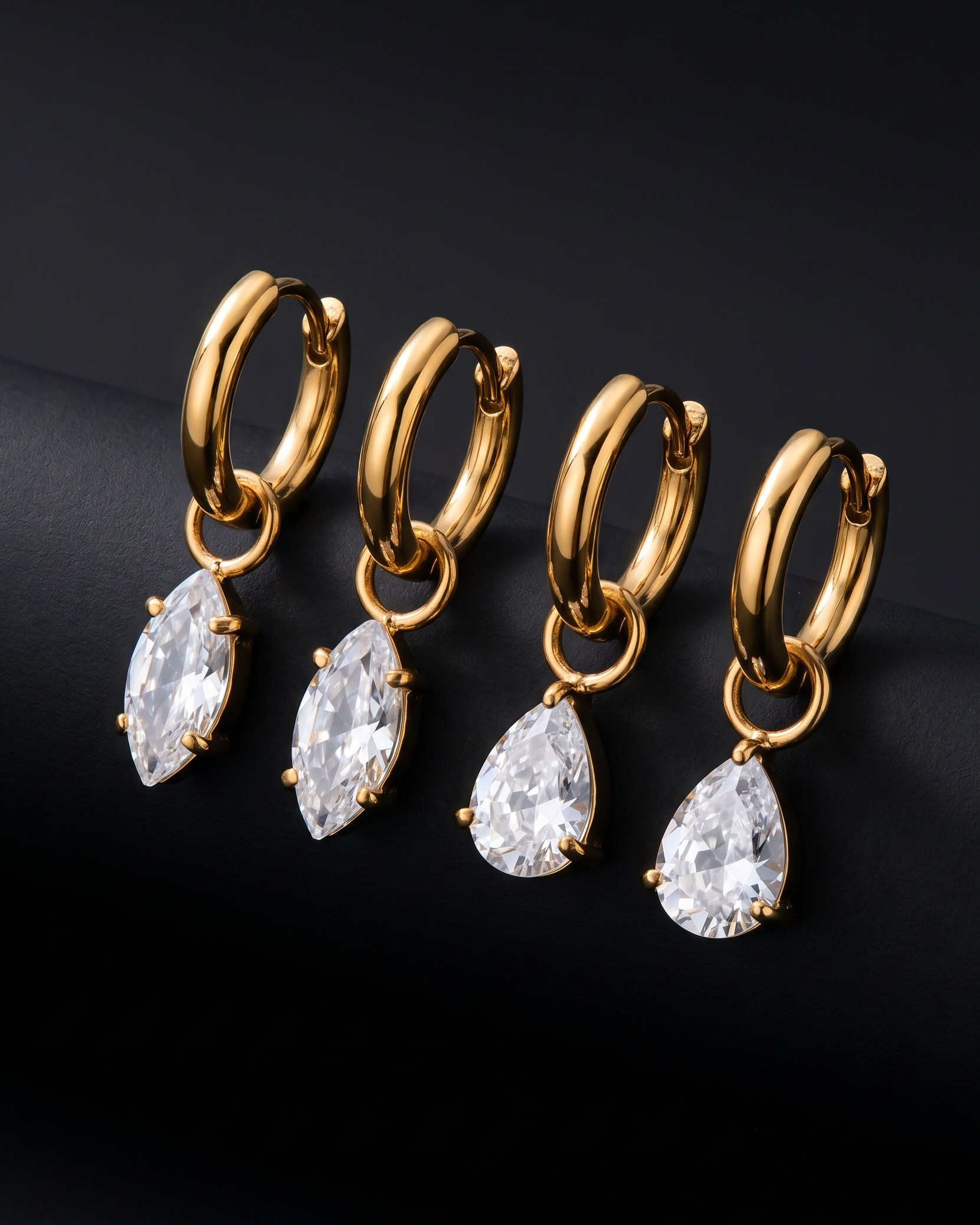 Gold hoop earrings with teardrop-shaped crystals on a black background