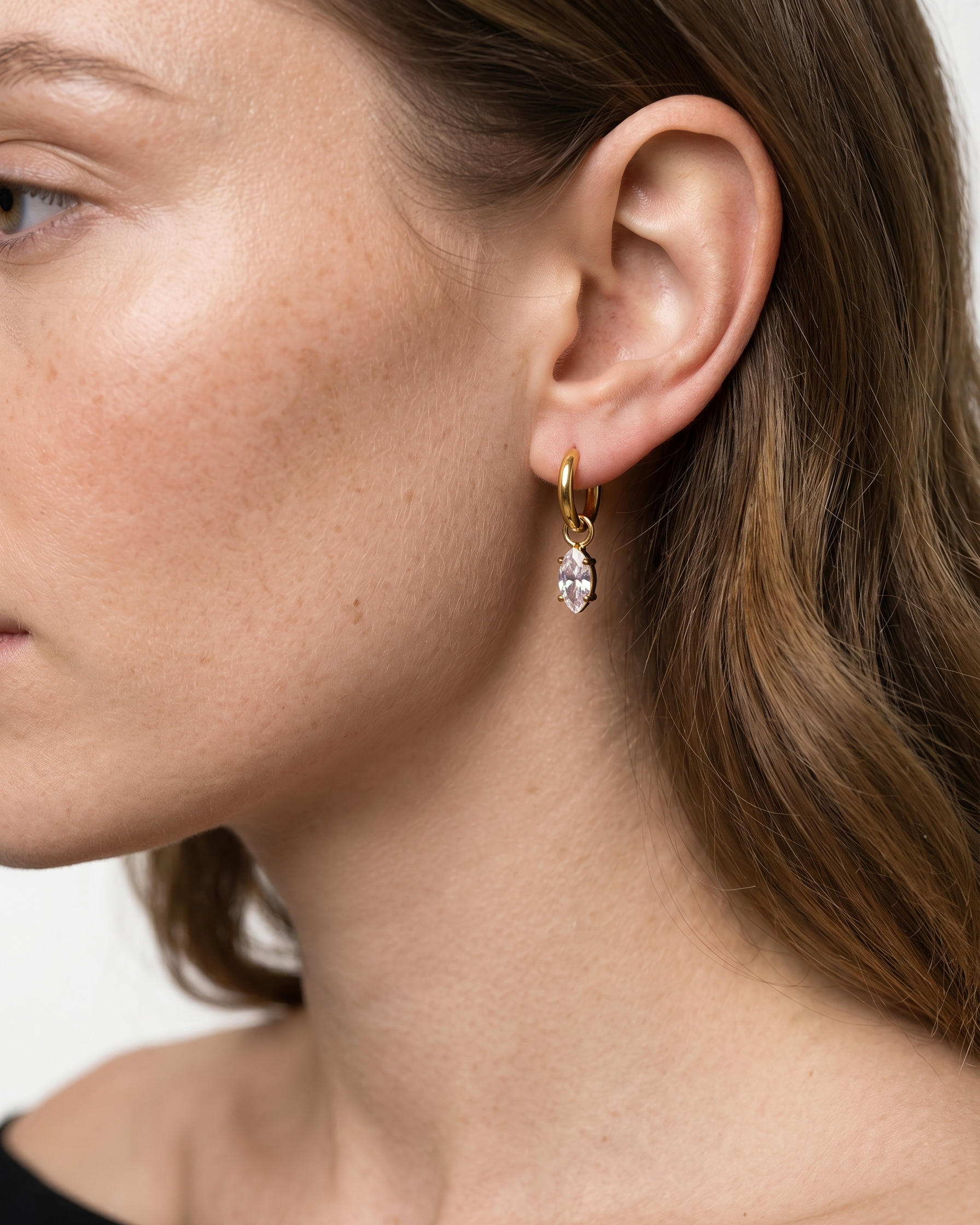 Close-up of a woman wearing a gold earring with a clear gemstone on a white background