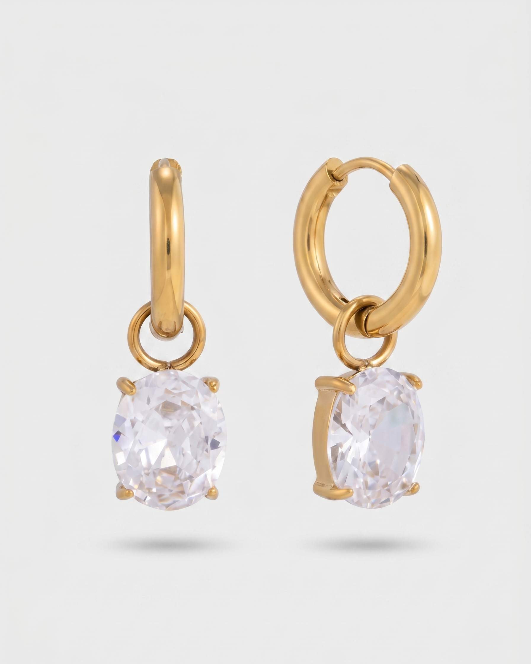 Gold hoop earrings with clear gemstones on a light gray background