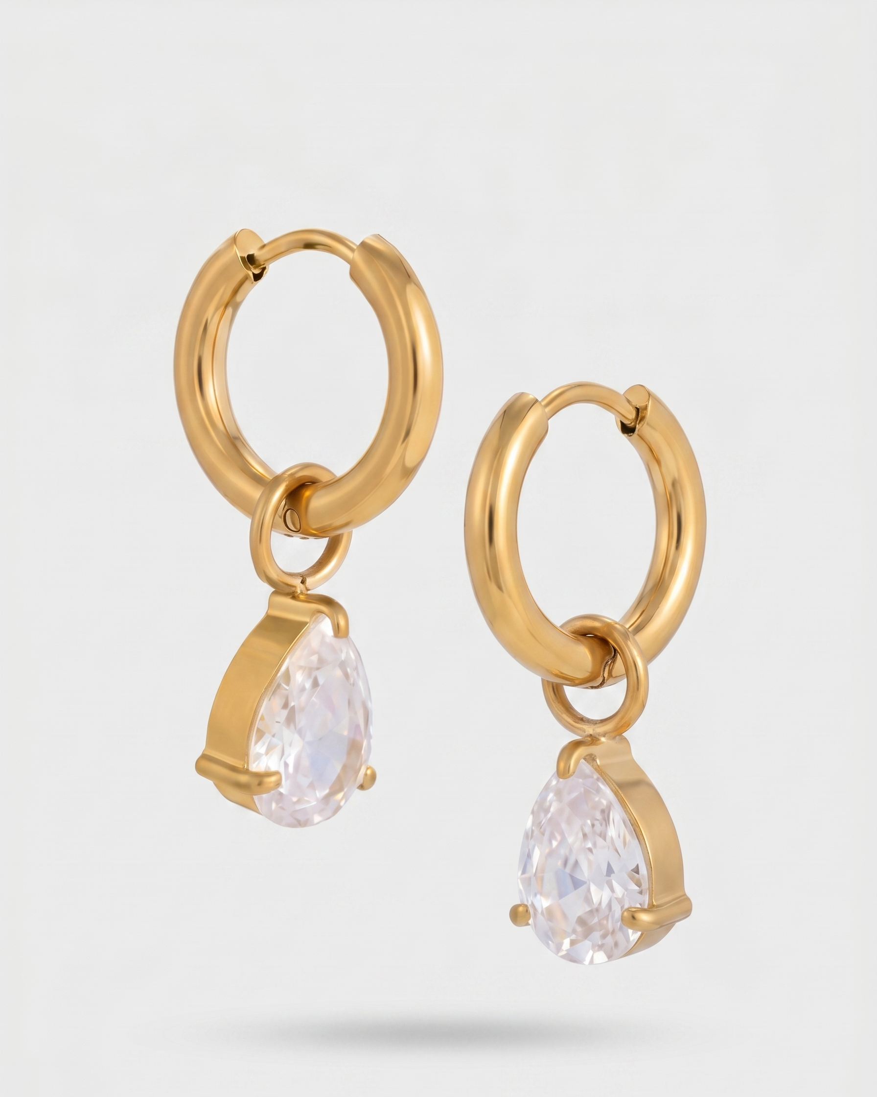 Gold hoop earrings with teardrop-shaped crystals on a light gray background